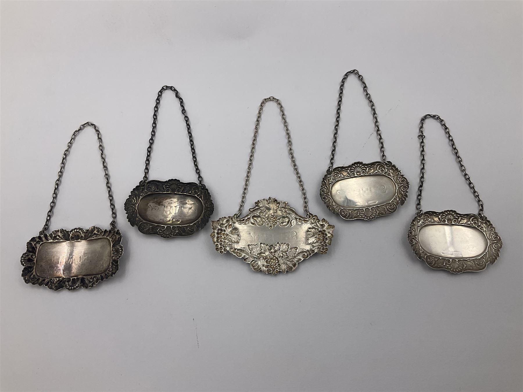 Five modern silver decanter labels, to include three similar Sherry and Brandy examples embossed with scrolls, two hallmarked C Robathan & Son, Birmingham 1989, and one hallmarked Laurence R Watson & Co, Birmingham 1987, together with a scotch example, hallmarked A Marston & Co, Birmingham 1970, and a larger sherry example, embossed with fruiting vines, hallmarked A Marston & Co, Birmingham 1993