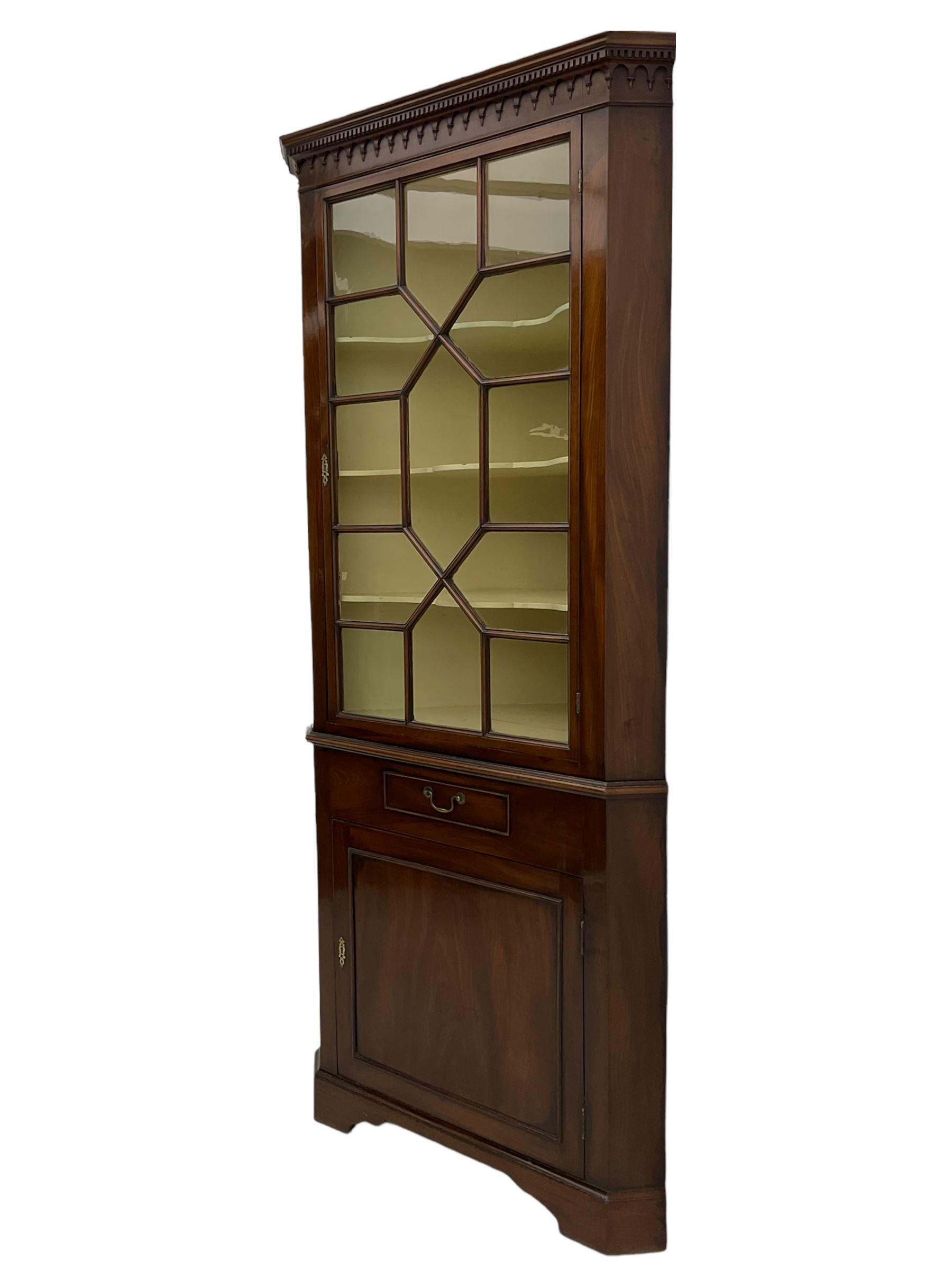 George III mahogany floor standing corner display cabinet, dentil cornice, upper astragal glazed door above small drawer and lower cupboard, on bracket feet, in two sections
