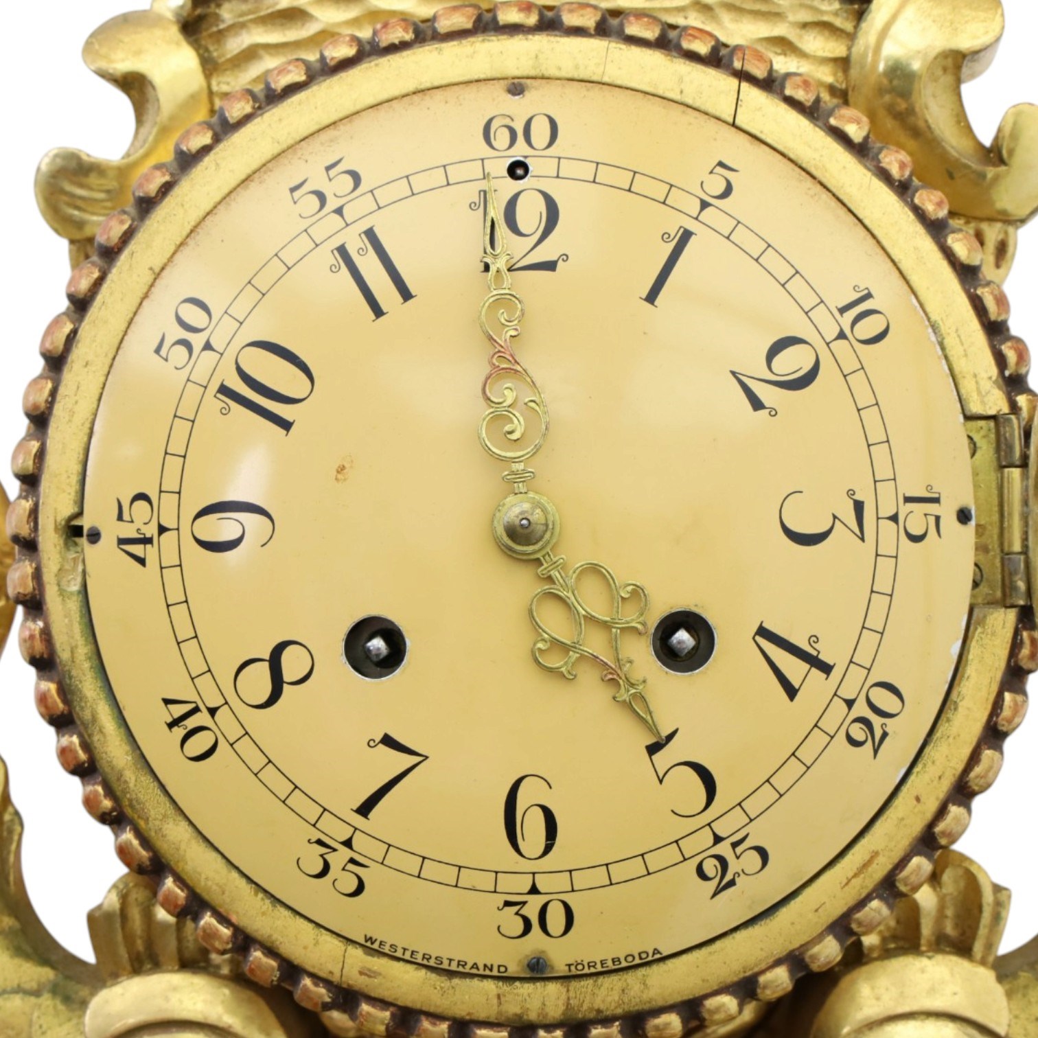 20th century Continental giltwood wall clock, circular dial with Arabic numerals and pierced gilt hands, within a carved case surmounted by a scrolling crest and flanked by stylised dolphins, above a shaped shelf with tassel pendants and a foliate terminal, pendulum missing