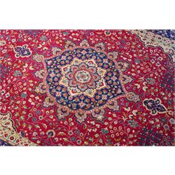 North West Persian Tabriz hand-knotted carpet, madder red field with a central cusped medallion issuing radiating pendants and an all-over design of scrolling arabesques, palmettes and flowering vinery enclosed by conforming spandrels, indigo main border of meandering floral vines and stylized palmettes, flanked by narrow guard stripes, cotton fringe ends 