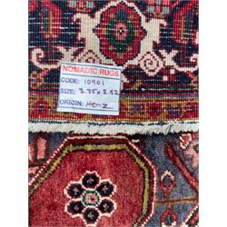 Northwestern Persian Heriz hand-knotted carpet, madder red field with a bold stepped medallion in indigo, ivory, and ivory, surrounded by angular floral motifs and stylized leaves, and the spandrels set within a dark border of rosettes and angular vine motifs, 335cmx252cm