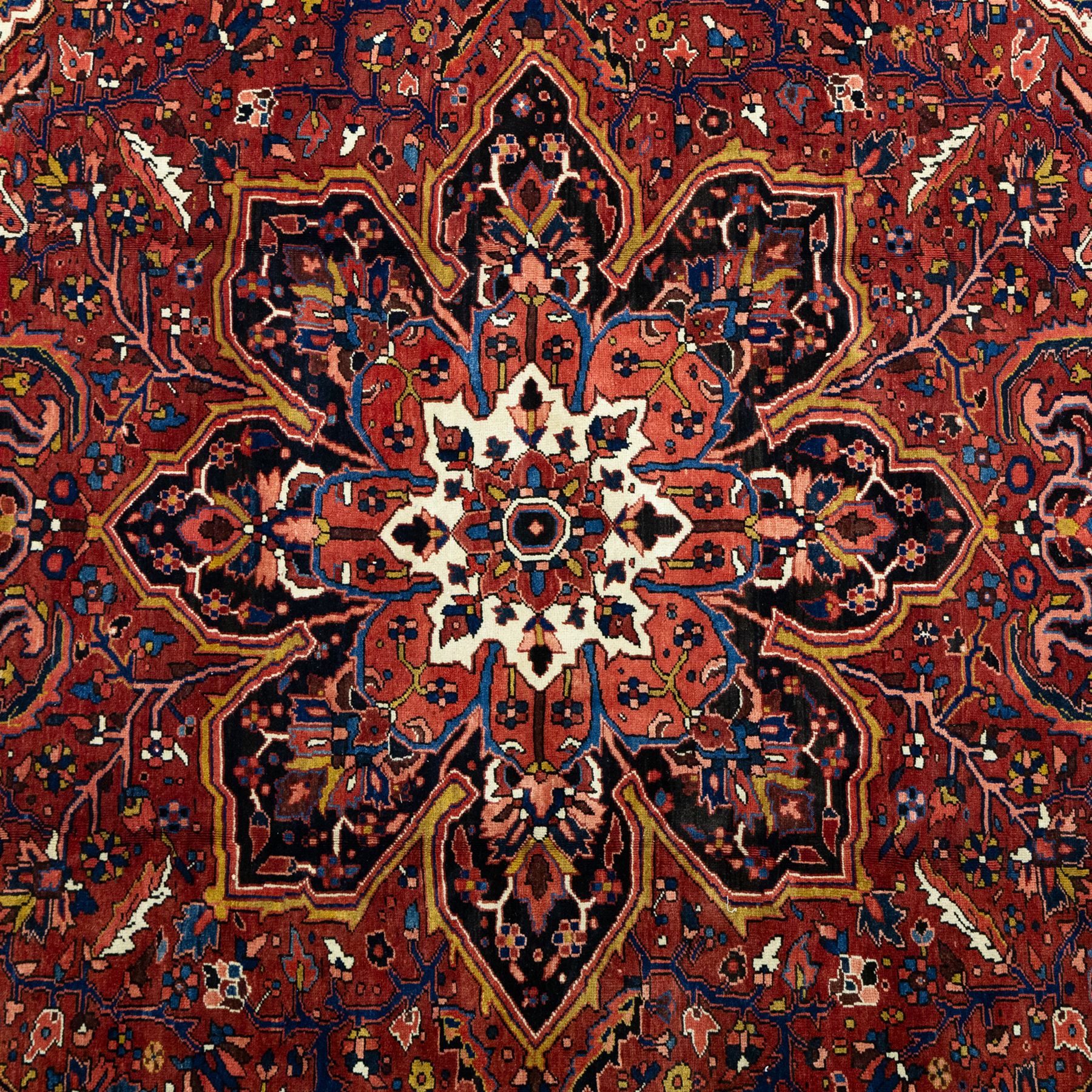 North West Persian Ahar hand-knotted carpet, madder red ground, with a large central shaped floral medallion with pendants, surrounded by angular scrolling foliate motifs incorporating rosettes, palmettes and stylised flowerheads, enclosed by ivory spandrels and a dark navy border with repeating floral motifs and meandering vines, flanked by narrow floral guard stripes, with cotton fringes