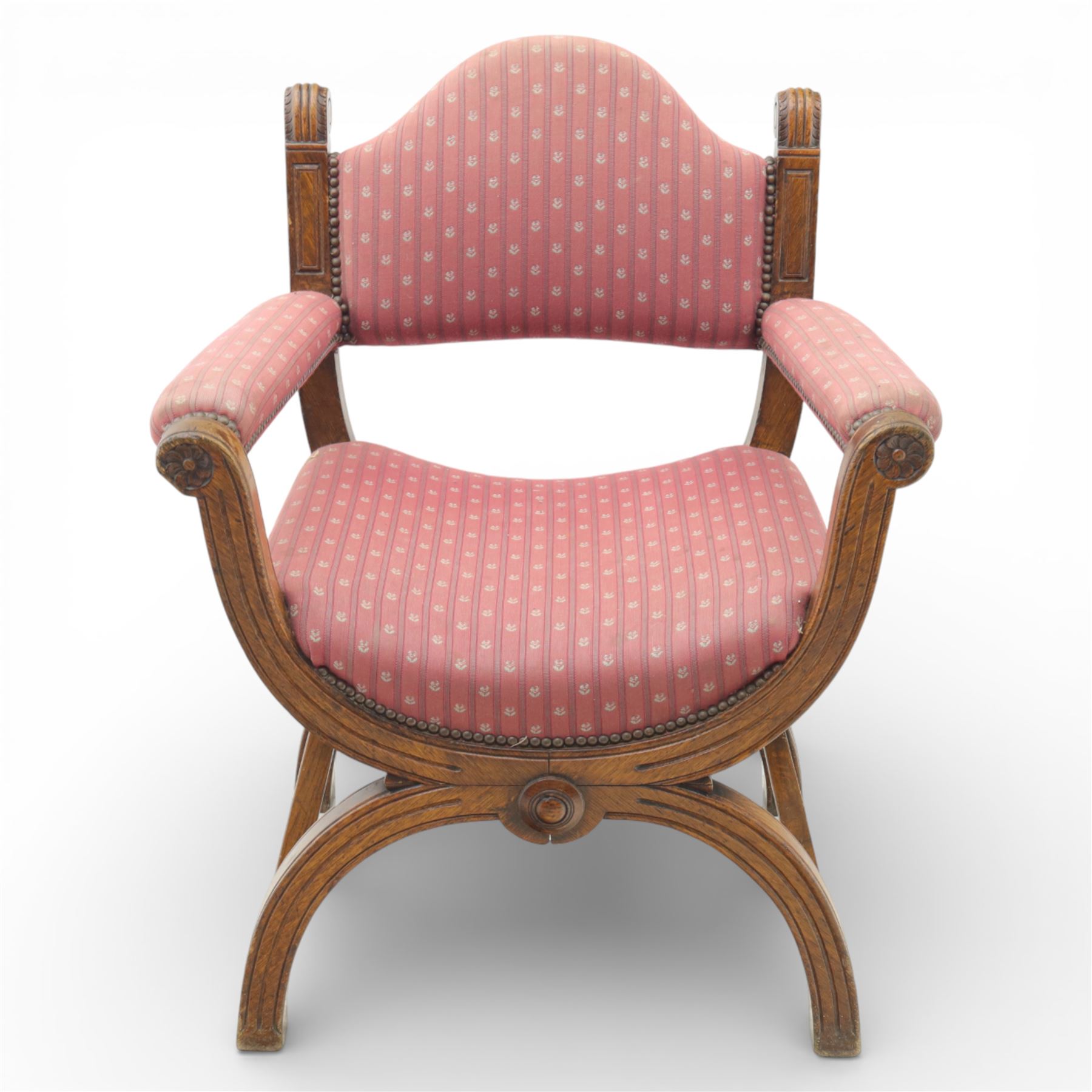 Late Victorian oak x-frame armchair, upholstered padded back and seat covered in pink patterned fabric with close studded borders, shaped downswept arms with scroll terminals, raised on curved x-frame supports with moulded scroll feet