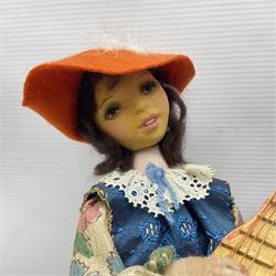 Anna Meszaros Hungary - three hand made needlework figurines - 'The Cobbler' as a child seated in a wooden rocking chair working on a removed boot H28cm; young girl in a long floral dress standing playing a harp H35cm; and young girl wearing a blue tabard standing playing a lute (3) Auctioneer's Note: Anna Meszaros came to England from her native Hungary in 1959 to marry an English businessman she met while demonstrating her art at the 1958 Brussels Exhibition. Shortly before she left for England she was awarded the title of Folk Artist Master by the Hungarian Government. Anna was a gifted painter of mainly portraits and sculptress before starting to make her figurines which are completely hand made and unique, each with a character and expression of its own. The hands, feet and face are sculptured by layering the material and pulling the features into place with needle and thread. She died in Hull in 1998.  