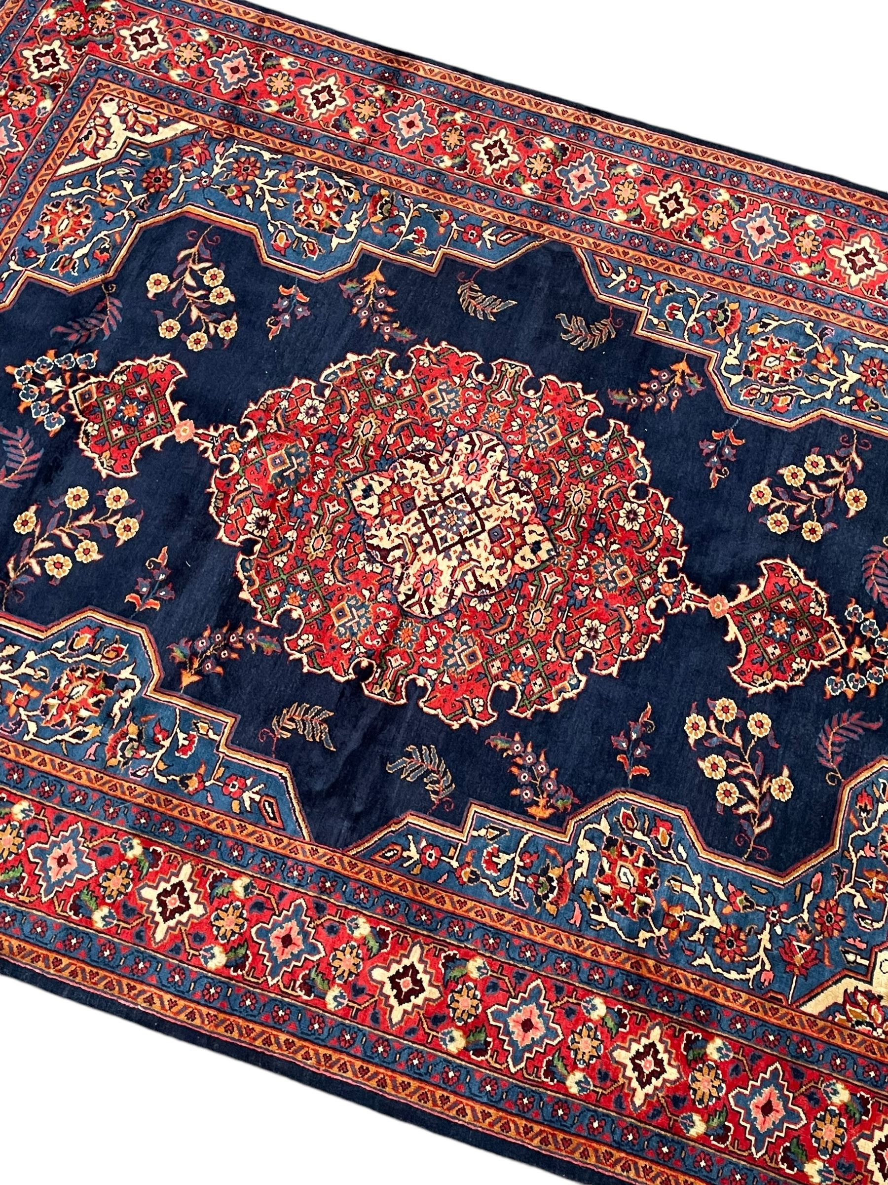 Persian Veis indigo ground carpet, the field with large pole medallion decorated with Herati motifs and surrounded by floral sprays, crimson ground border with repeating cross motifs and stylised flower heads, within guard stripes 