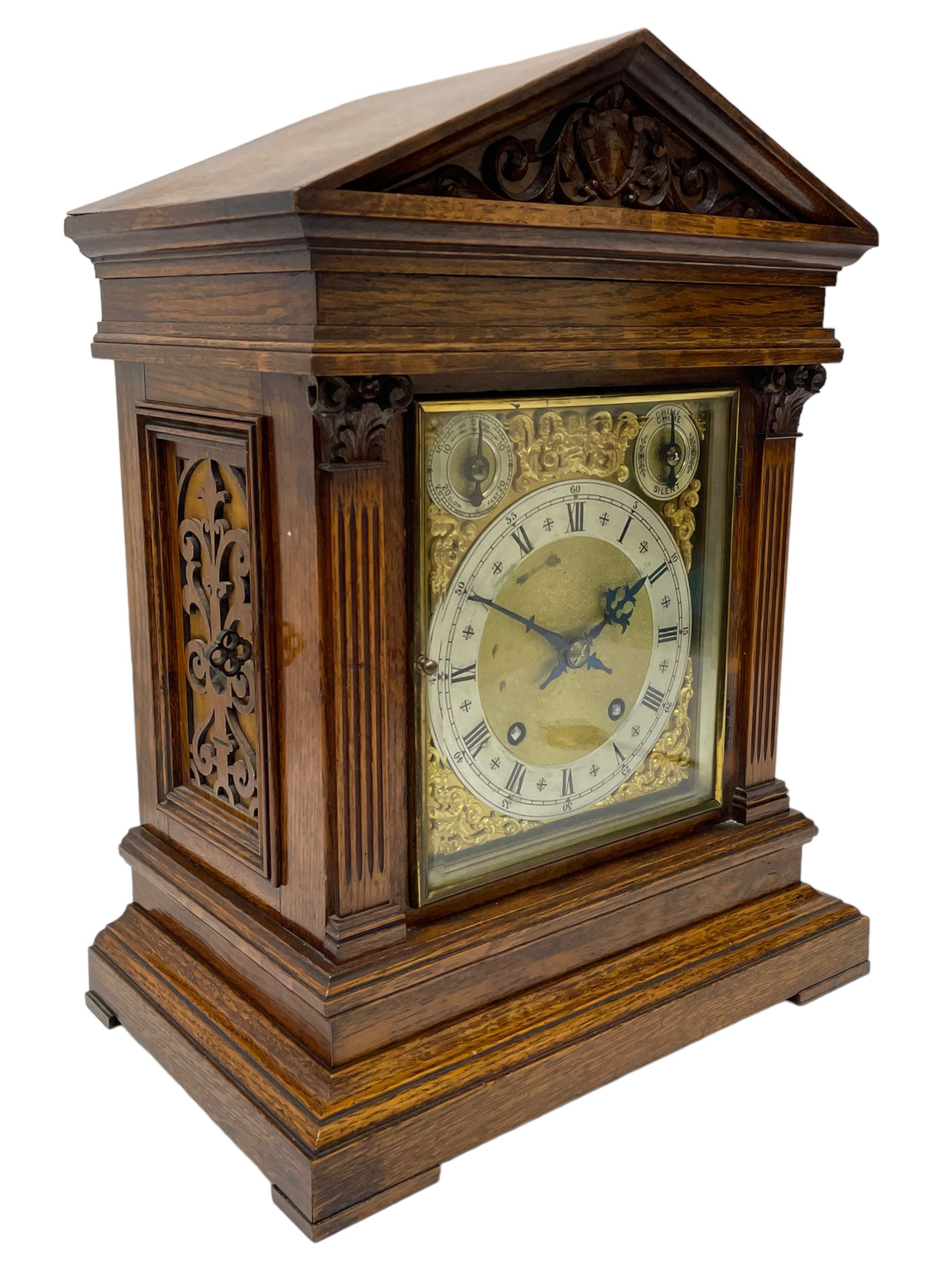 Winterhalder & Hofmeier- German 8-day oak cased mantle clock, in an architectural styled case with a gable pediment and recessed carving to the tympanum, square brass dial flanked by carved reeded pilasters and capitals, with open carved silk backed sound frets on a shaped plinth with padded feet, brass dial with cast spandrels and silvered chapter, Roman numerals, minute track and stylised gothic hands, conforming chime/silent and pendulum regulation dials, twin train going barrel movement with quarter-hour striking on two coiled gongs and the hours on one.
With pendulum.