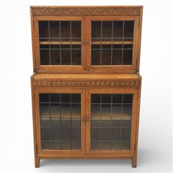 Early 20th-century Arts and Crafts glazed oak bookcase, upper section fitted with a pair of leaded glazed doors enclosing a fixed shelf above a projecting frieze drawer interior with baize-lined writing surface flanked by two compartments, carved with interlaced decoration, lower section fitted with a further pair of leaded glazed doors enclosing a single shelf, raised on short stile feet 