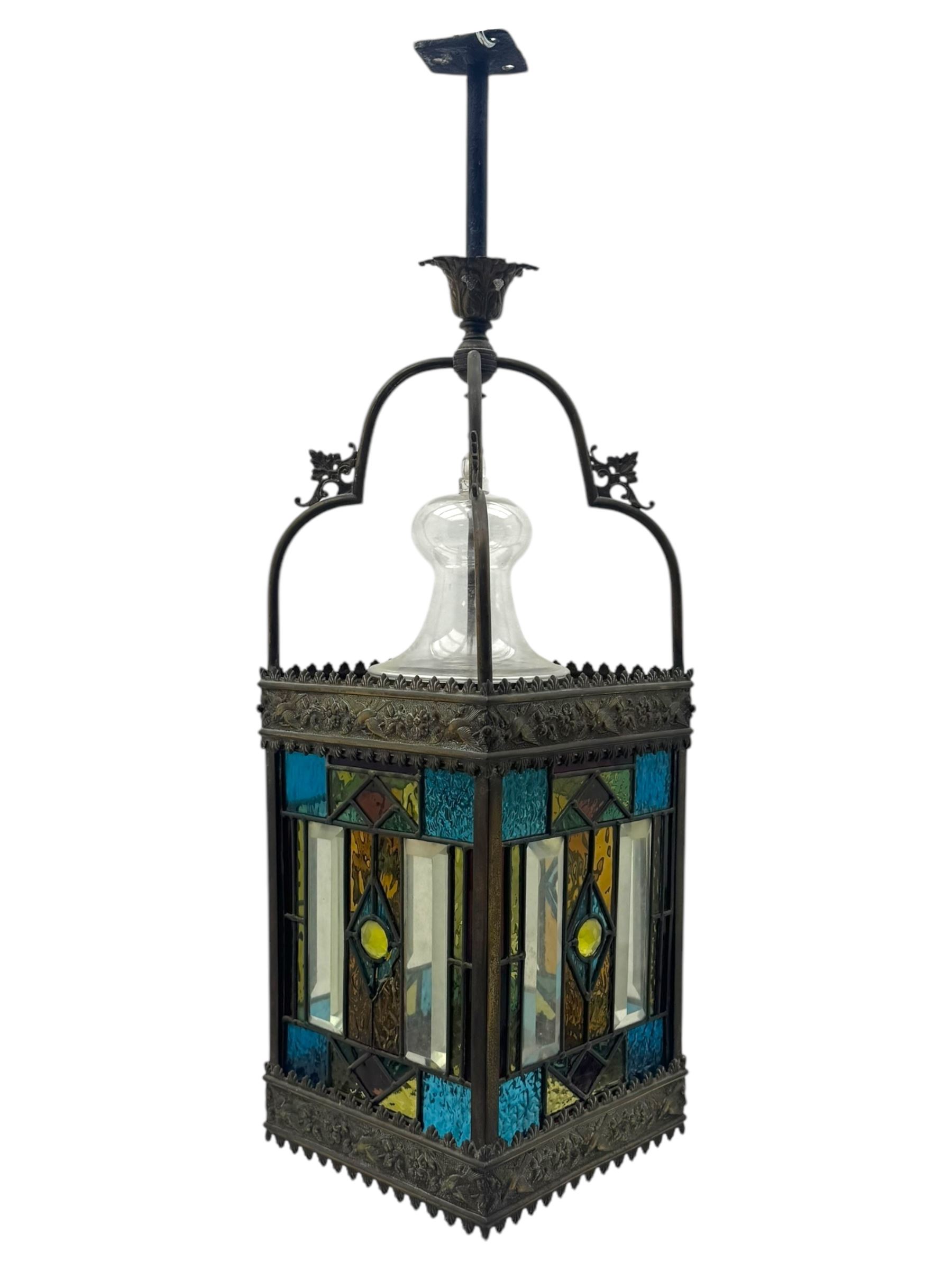 20th century Gothic design stained glass and brass hall lantern, with ornately decorated frieze and apron, with geometric coloured glass panels and eight rectangular bevelled glass panels, with bell shade, wired for electricity 