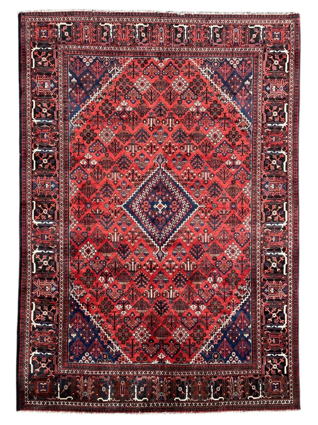 Persian Joshaghan crimson ground rug, stepped lozenge medallion surrounded by repeating foliate lozenge motifs, the border decorated with stylised plant motifs, within geometric guard stripes