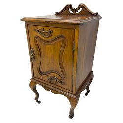 Edwardian Art Nouveau walnut bedside cabinet, raised broken swan neck back with carved flower heads, single fielded panelled door enclosing single shelf, raised on cabriole supports with ceramic castors