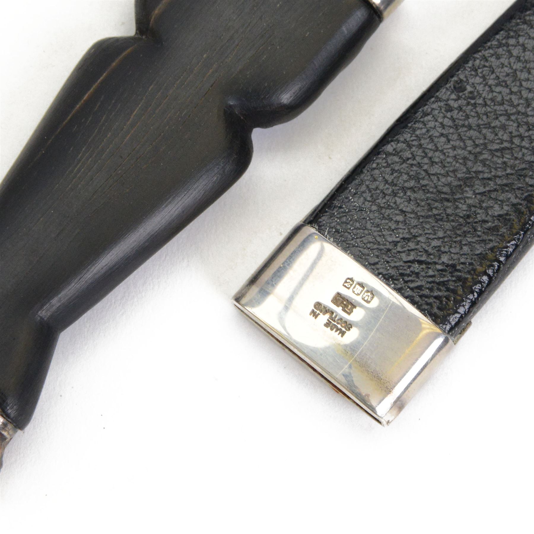 Skean dhu, the 9cm blade with scalloped back edge, with ebonised hilt and stone pommel, in its leather covered sheath with silver collar, hallmarked 1955