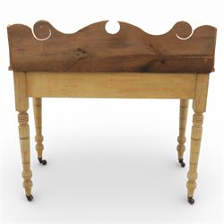 19th century stripped pine side table, the rectangular plank top with low shaped back rail incorporating scroll cut ends, fitted with two frieze drawers with ceramic knob handles, raised on turned supports terminating in castors