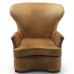 20th century tan leather armchair, the curved wing back above low square arms, shaped loose seat cushion with piped edge, close-nailed side detail, raised on concealed castors