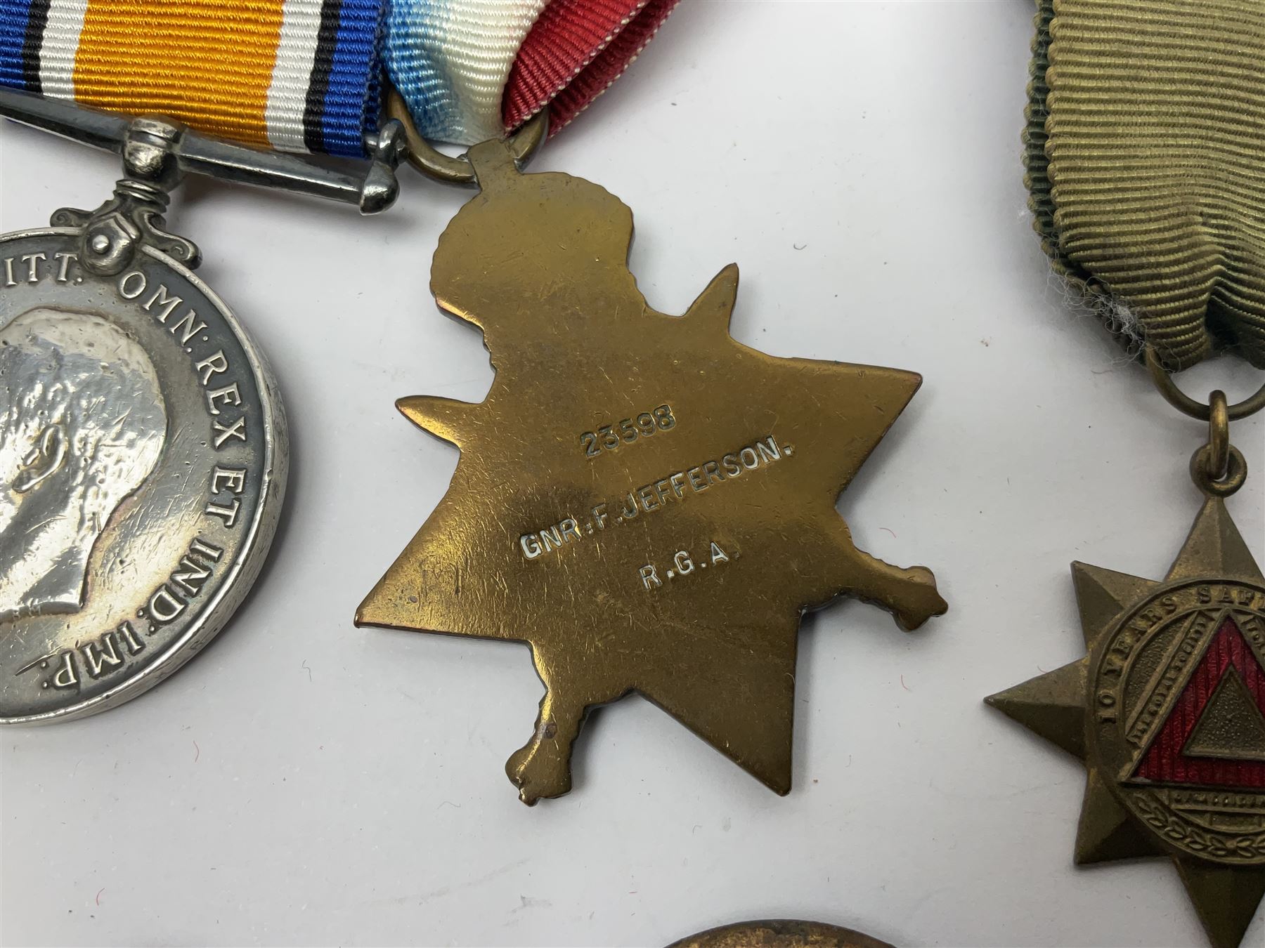 Made-up group of three WWI medals comprising 1914 Star awarded to 23598 Gnr. F. Jefferson R.G.A., British War Medal and Victory Medal with names removed; with ribbons on wearing bar; 1942 Motorist's Medal and small quantity of cap badges, Royalty badges etc