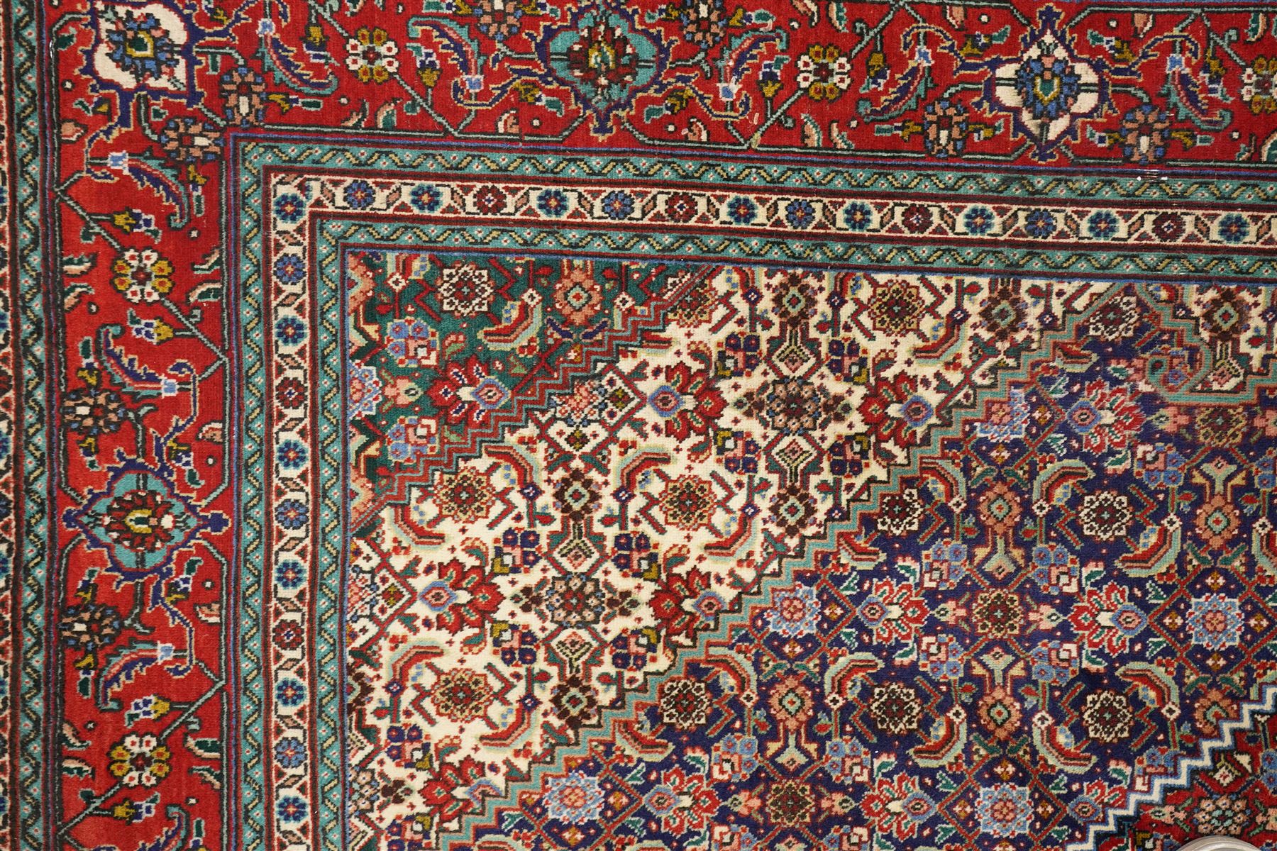 North West Persian Tabriz hand-knotted rug, ivory field with a central lozenge shaped medallion in indigo and madder red, issuing an ornamented arrangement of Herati style motifs, rosettes and angular floral elements, conforming spandrels on an ivory ground, main border in madder red with stylized vinery and palmettes, flanked by multiple guard border, with cotton fringe ends 