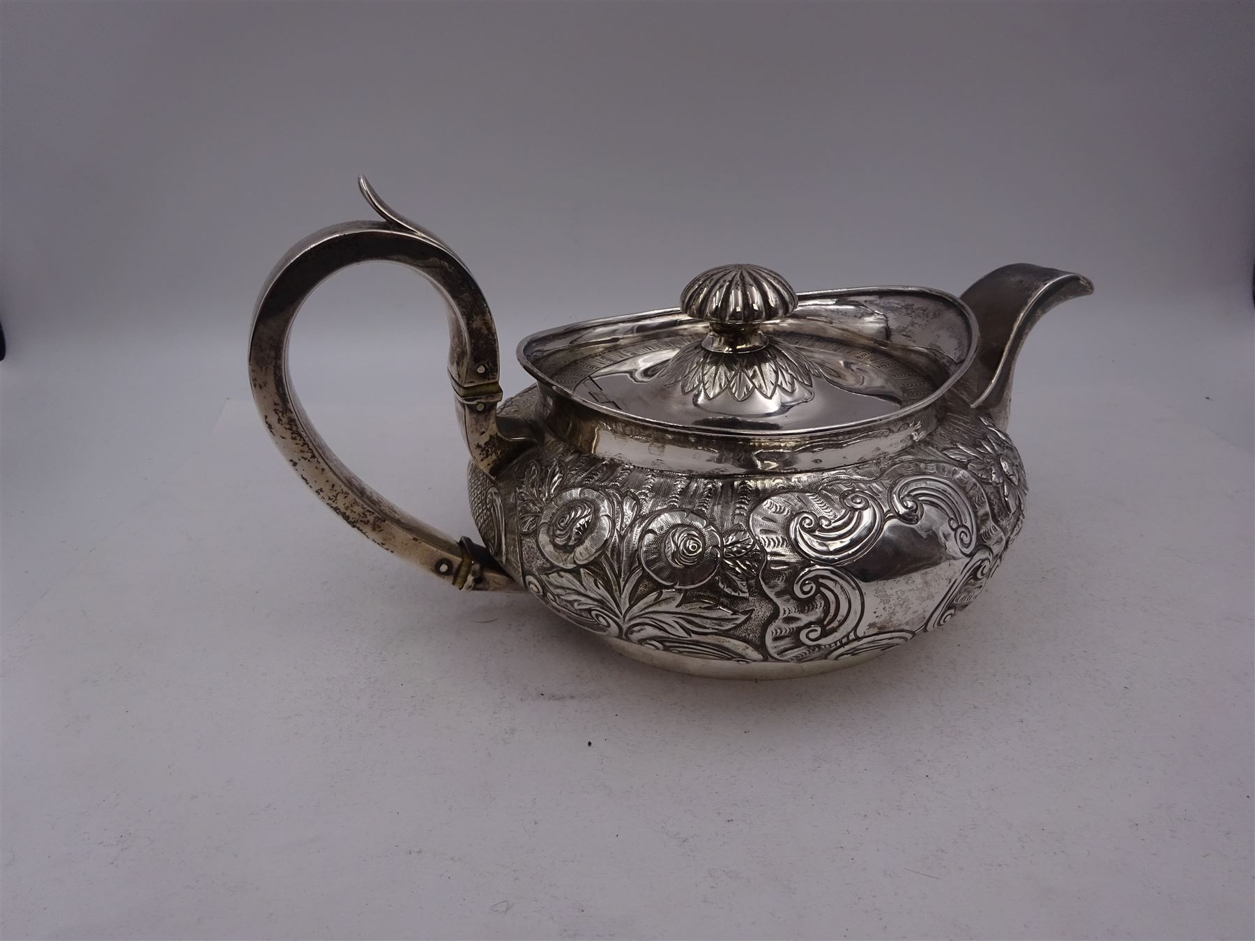George III Irish silver teapot, of squat circular form, the body with repousse and chased floral and C scroll decoration, with capped C handle and ivory insulators, engraved to base 'Presented to Troop Sergeant Major John Percival, of the 4th Dragoon Guards by Alex D. Tait, Esq, late Captain in that corps as a mark of approbation of his steady and upright conduct when Sergeant Major of his Troop, Dublin, June 2nd 1843', hallmarked William Law, Dublin 1817, H12.5cm, This item has been registered for sale under Section 10 of the APHA Ivory Act