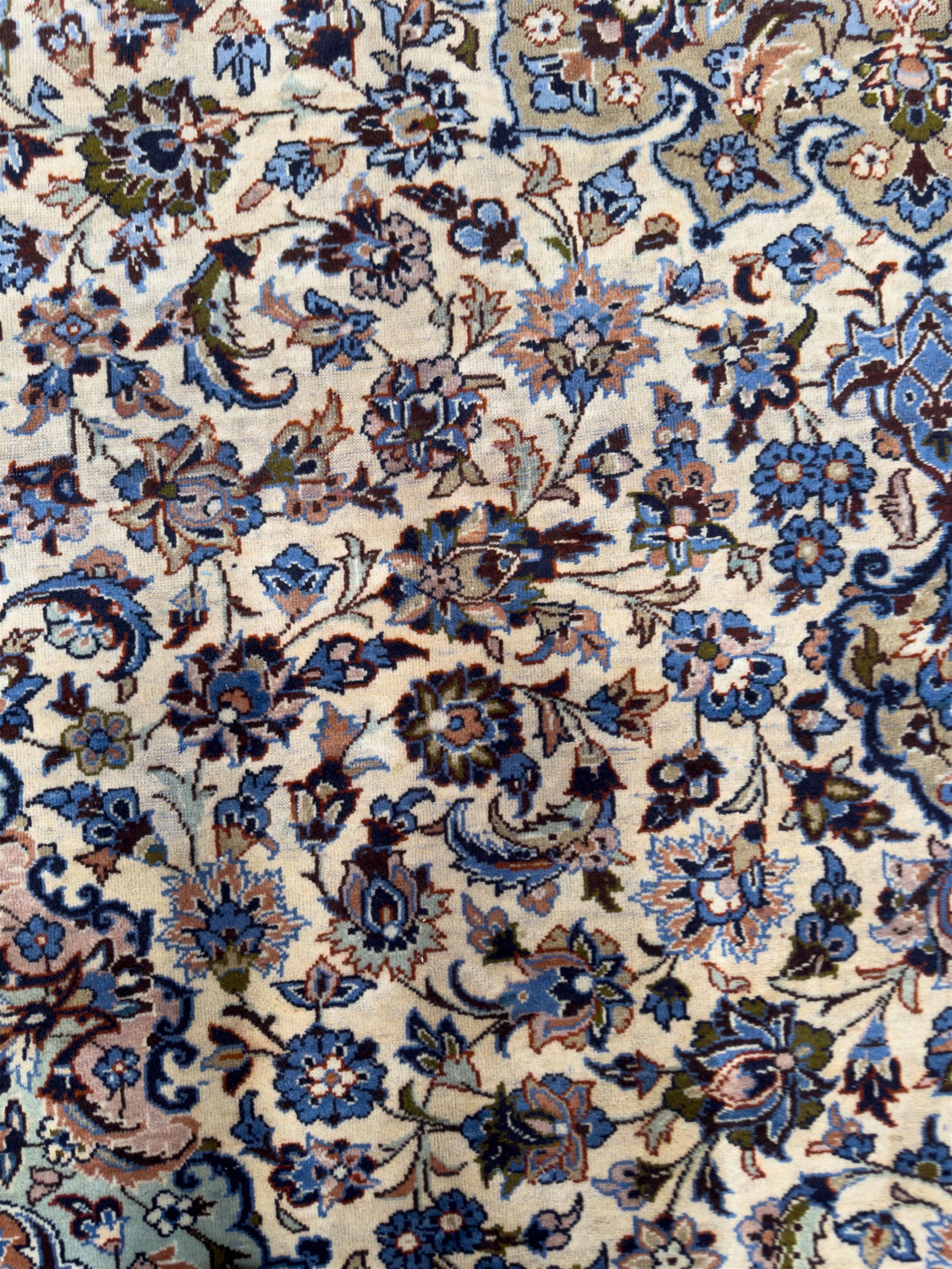 Central Persian Najafabad hand-knotted carpet, the ivory field with a central floral medallion radiating palmettes and arabesques in tones of blue, lilac and tan, enclosed by a wide navy border of scrolling vine and rosette motifs, with red spandrels and multiple guard stripes