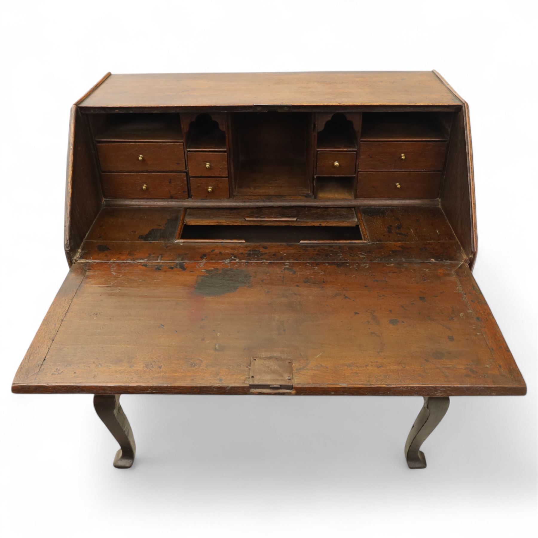 Early 18th century George I oak bureau on original stand, the fall front enclosing an arrangement of correspondence drawers and pigeonholes over central well, fitted with single long drawer below, the shaped apron over cabriole supports with pad feet