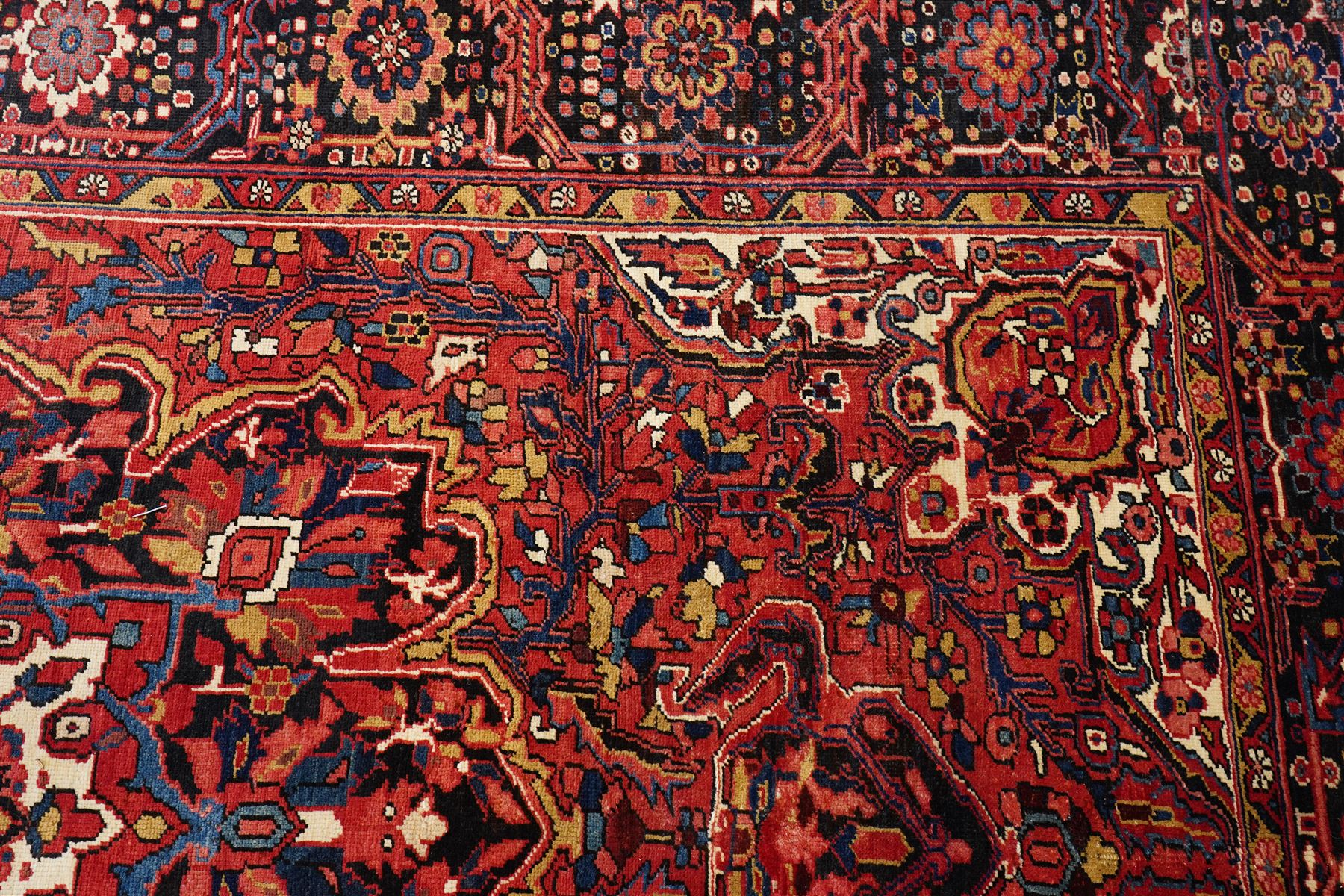 North West Persian Heriz/Ahar hand-knotted carpet, brick-red field with a large central angular stepped medallion with pendant motifs, surrounded by stylized palmettes, serrated leaves and geometric floral devices , ivory corner spandrels, enclosed by a dark indigo main border of stylized rosettes and angular vine motifs, between multiple guard stripes, with cotton fringe ends 