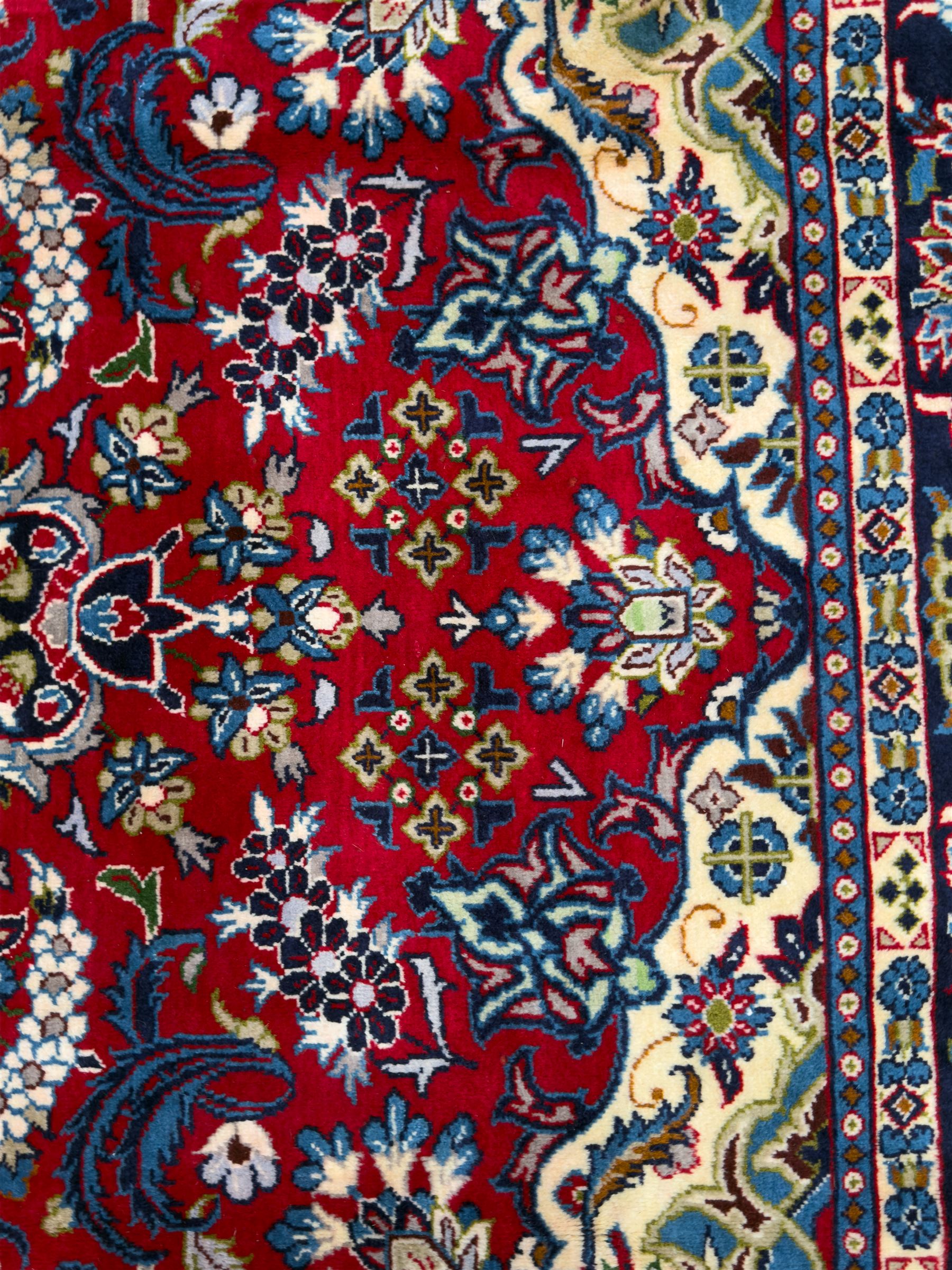 Central Persian Isfahan Carpet, hand-knotted, featuring a bold central rosette medallion on a rich red field, flanked by stylised floral sprays, scrolling foliage and mythical animals, within a broad indigo border decorated with alternating cartouches and flowerheads
