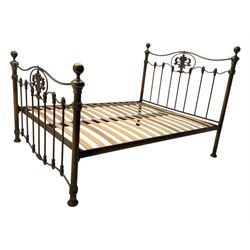 Victorian design king size brass bed frame, featuring an arched headboard and footboard with intricate cast floral and scrollwork centre motifs, flanked by cylindrical supports with ball finials and decorative collars, raised on rounded feet, with a slatted wooden base