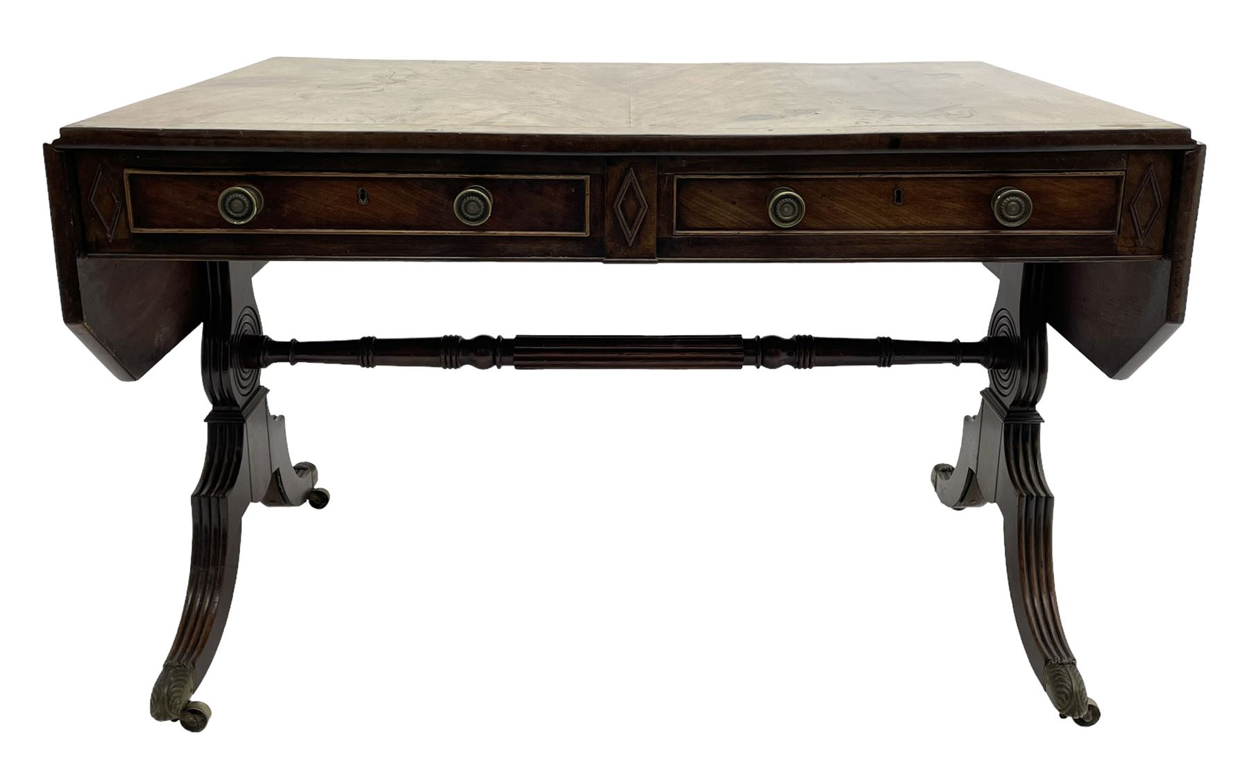 Regency mahogany sofa table, canted rectangular drop leaf top with walnut crossbanding, fitted with two frieze drawers with central lozenge decoration, two opposing false drawers, vasiform end supports with reeded edge and central roundel joined by ring turned and reeded stretcher, splayed supports on scaled brass cups and castors