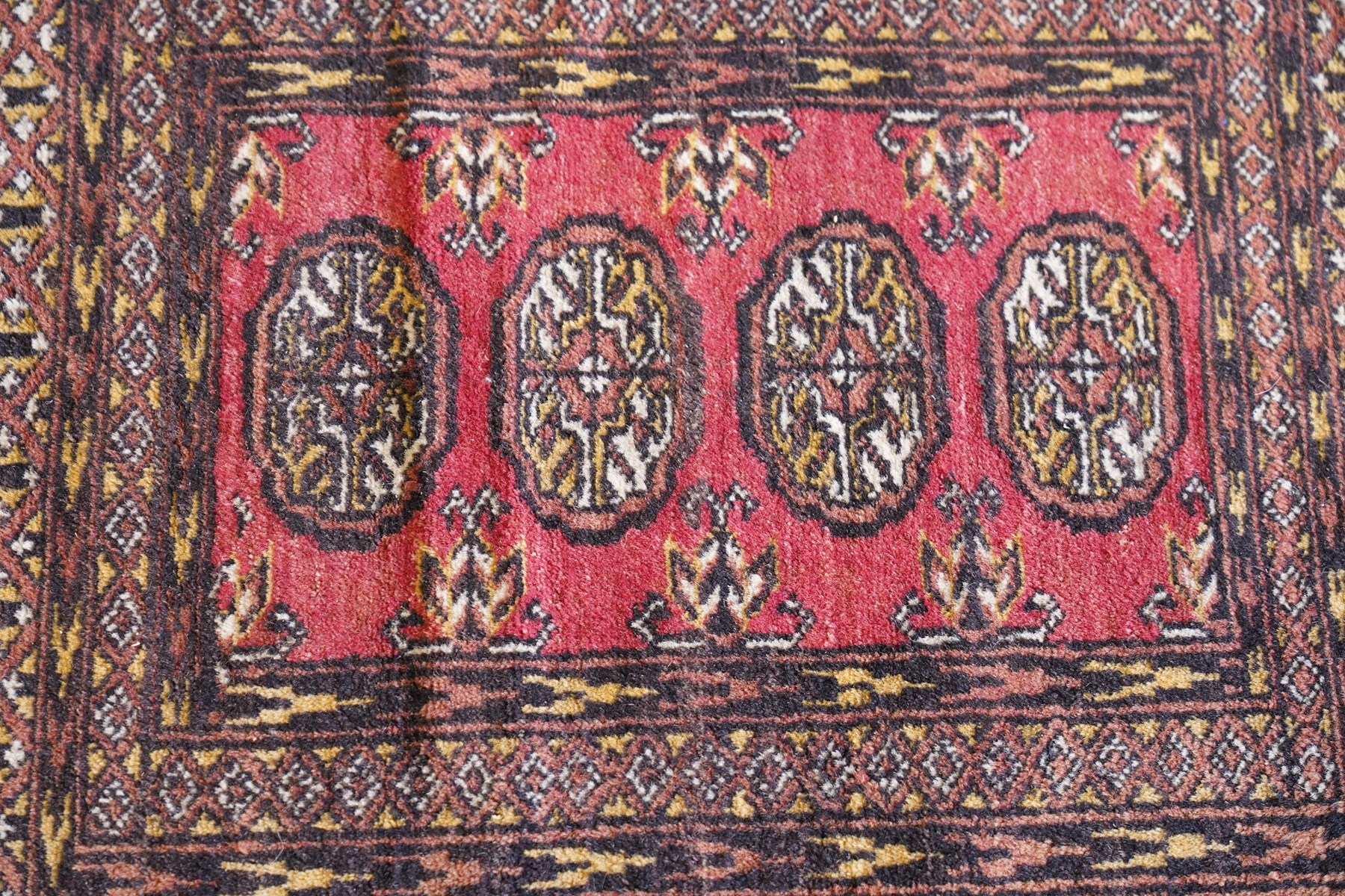 Four small Persian and Caucasian design rugs, comprising a Kazak rug with twin hooked medallions on a red ground, Baluchi rug with geometric motifs on a muted red ground, Shiraz rug with a central ivory and red medallion on a blue ground, and a Bokhara mat with four guls on a rose ground, each enclosed by geometric borders, largest 143cm x 88cm (4)