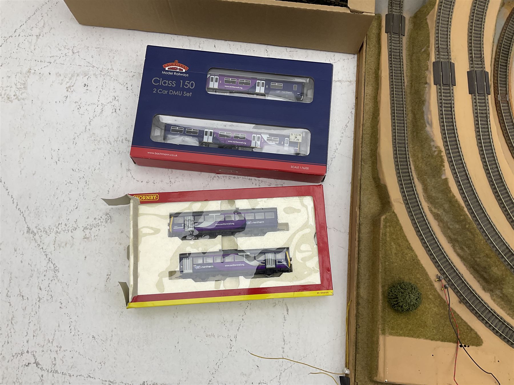 '00' gauge - table-top moulded plastic model railway layout with various rocky outcrops, tunnels, waterfall to lake, loops of Fleischmann track supplemented by Hornby track, bridges, kit built buildings and other accessories; together with Bachmann Class 150 2-car DMU Set and Hornby Northern Rail Class 142 2-car Set; both boxed; and small quantity of other rolling stock, three controllers etc  200 x 120cm