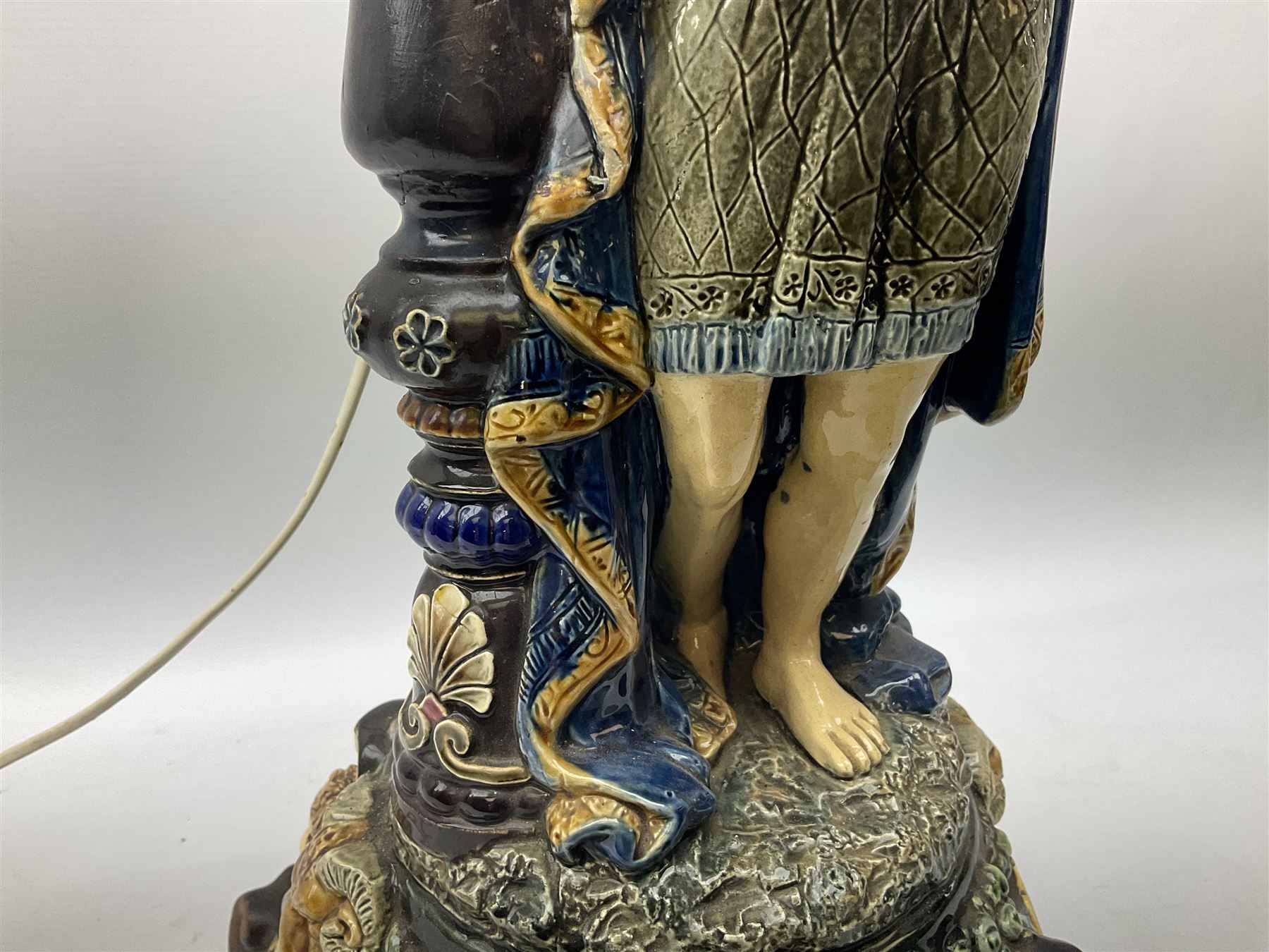 Composite table lamp modelled as a Roman Emperor donning blue robes, upon quatrefoil base modelled with rams heads and winged cherubs, H56cm excl fitting