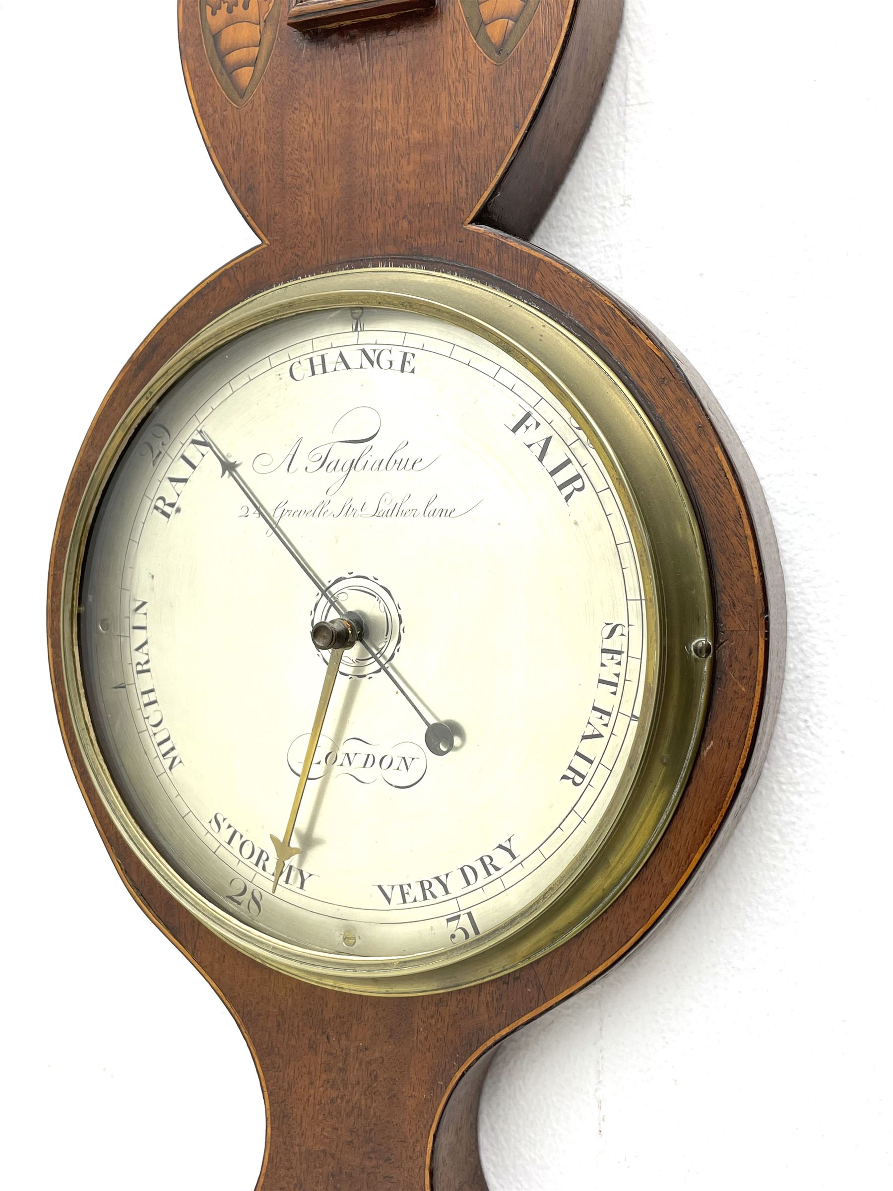 Early 19th century William IV mercury wheel barometer with a rosette inlaid broken pediment and correspondingly inlaid round base, mahogany veneered case with inlaid oval conch shell paterae and satinwood stringing to the edge, with an arched thermometer box and spirit thermometer measuring degrees Fahrenheit from 20 to 120, eight-inch silvered register reading barometric pressure in inches from 28  to 31, with predictions in Roman upper and lower case and script, dial inscribed “A Tagliabue,24 Grenville Street, Luther Lane, London”, with a steel indicating hand, brass recording hand and cast brass bezel.