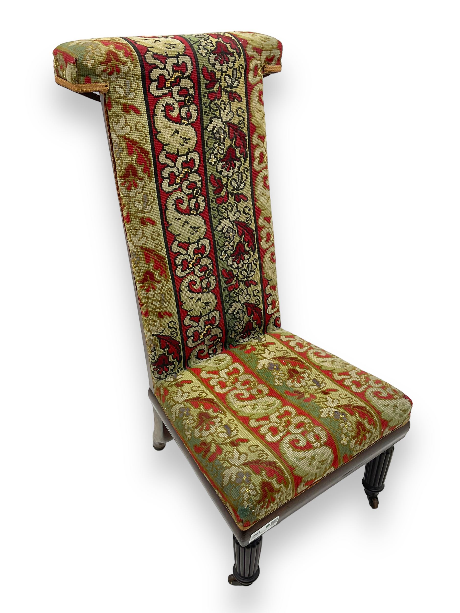 19th century mahogany framed prie-dieu chair, upholstered in red and green patterned fabric, high back with rolled top, standing on turned front supports with castors