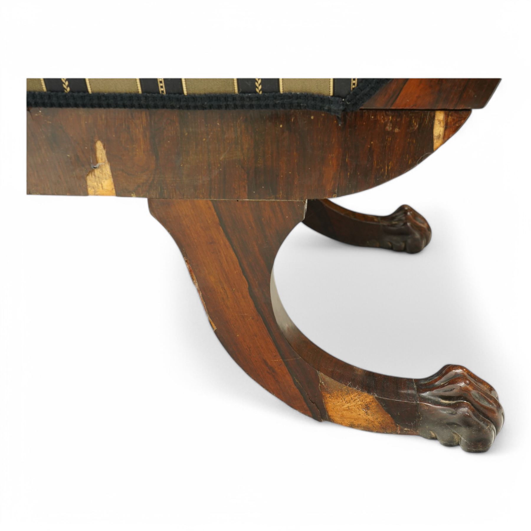Regency brass inlaid rosewood chaise lounge or settee, shaped back over rolled head and foot, upholstered in black and gold striped fabric with rectangular squab cushion and bolster cushion, the rolled terminals carved with acanthus leaf roundels, lower rectangular foliate carved panels, on out splayed supports with paw carved feet 