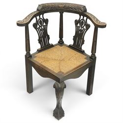 Pair of 19th century carved oak corner chairs, cresting rail carved with central floral bouquet with trailing foliage extending to the scroll arm terminals, pierced back splats with rosette motifs over drop-in rush seats, front cabriole support with acanthus carved knee and ball-and-claw foot