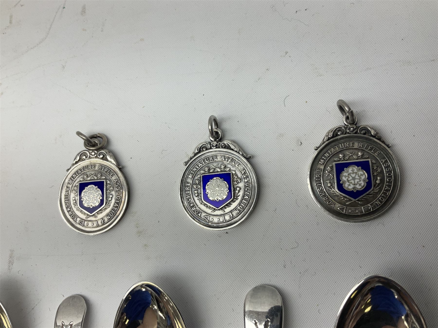 Set of three Yorkshire Miniature Rifle Association hallmarked silver and enamel fob medals, Birmingham 1925, 1926 & 1929; together with six silver plated coffee spoons each engraved with crossed rifles to the terminal (9)