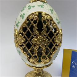 Franklin Mint The Emerald Isle Collector Egg, the egg decorated with embossed shamrocks upon a cream ground, with a gilded shamrock finial, accents and openwork door, opening to reveal a miniature landscape scene, upon three gilded feet set with green paste stones, with certificate of authenticity H23cm, 