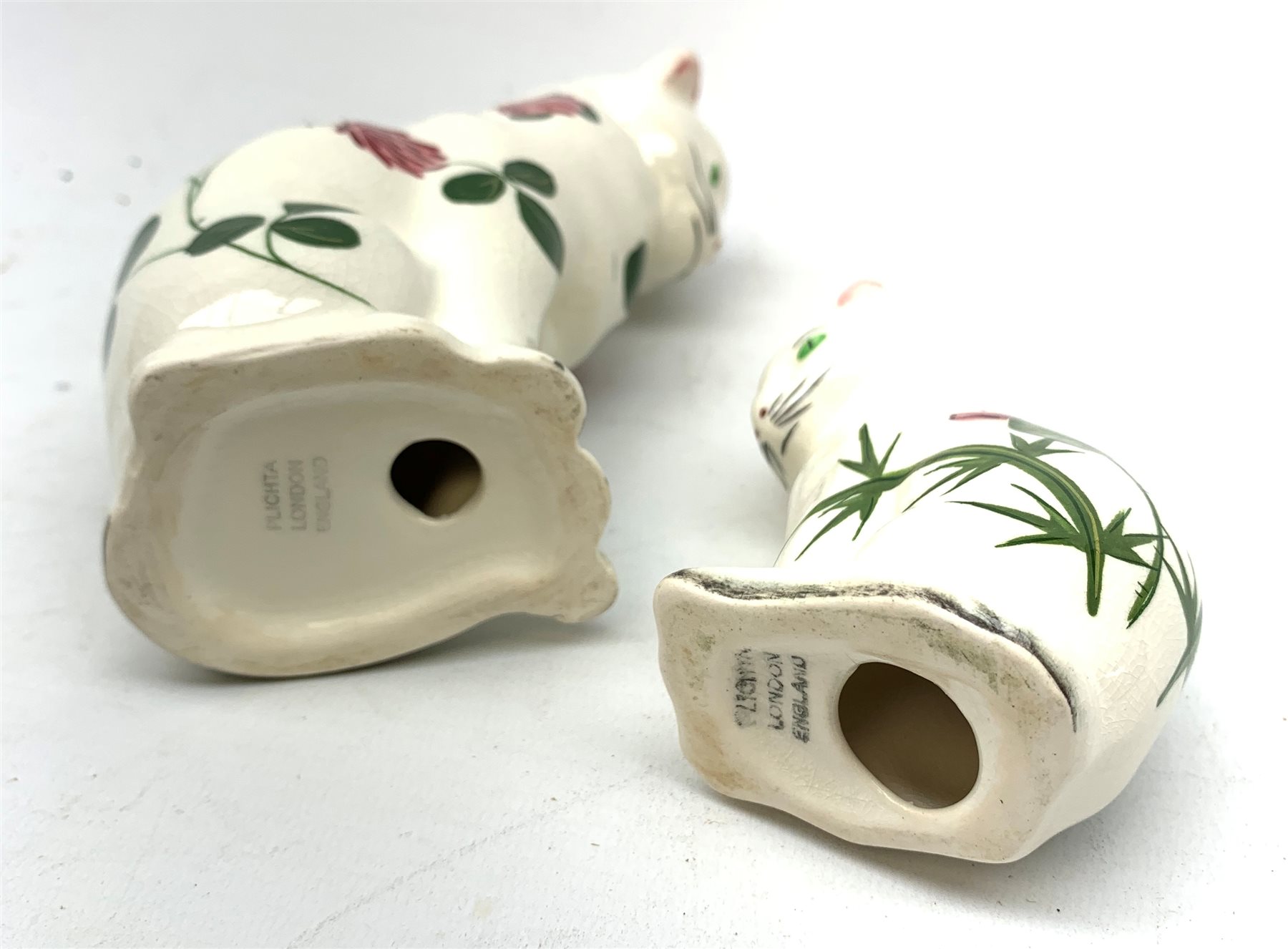 Two Plichta pottery cat figures, the largest example hand painted with clover leaves and flowers, with printed mark beneath, H14cm, the smaller example hand painted with thistles, with printed mark beneath, H8cm. 