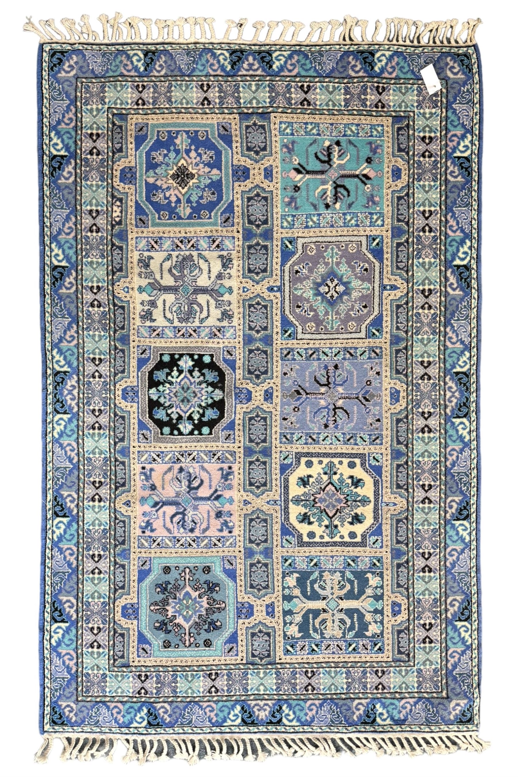 Morrocan single weft blue ground rug, the field segmented into a grid of ten rectangular panels, bordered by a series of guard bands with repeating floral and geometric patterns with interlocking vines and rosettes, the edges finished with a fringe of twisted tassles