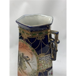 A pair of Japanese Nippon Kinjo vases, of tapering hexagonal form with twin stylised handles, the cobalt blue ground with oval hand painted panels to front and verso depicting landscapes, further detailed with smaller floral bands and panels and heightened with gilt, each with mark beneath, H30.5cm.  