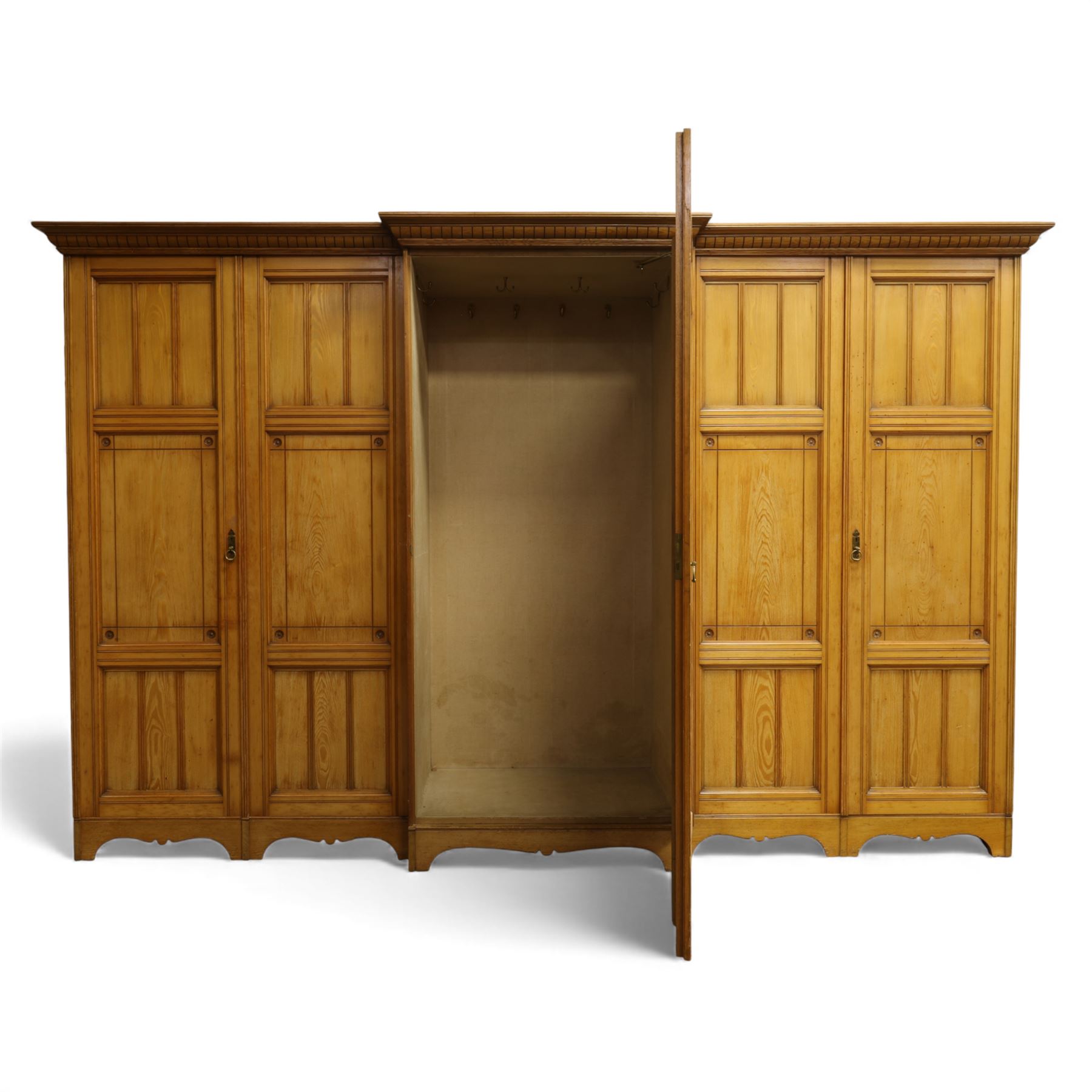 Gothic revival ash breakfront wardrobe in the manner of Charles Bevan, the four fielded panelled doors flanking a central mirrored door, opening to reveal an fitted interior with hanging rails and compartment shelves and drawers, upon a shaped plinth base with bracket cut feet

