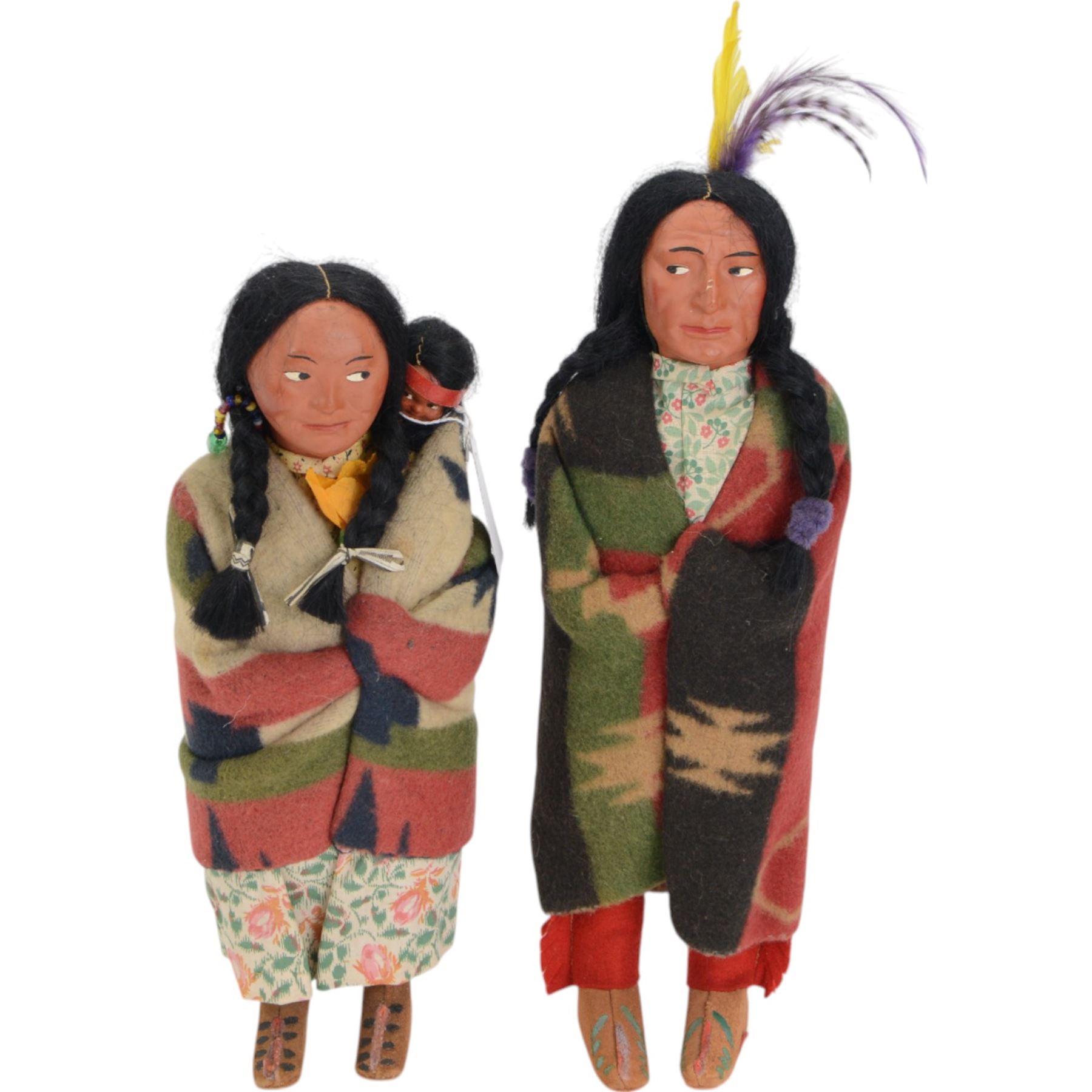 Two Skookum Native American Indian dolls with foot label, with painted composition heads, side glancing eyes, black hair wig, stuffed rigid body, original clothes, the male with feather headdress, the female with baby on back, H32cm