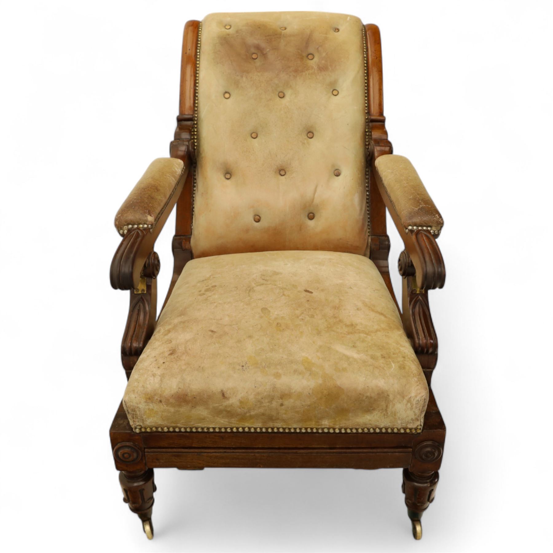 William IV mahogany gentleman's library reclining armchair, leather button upholstered and brass-studded back and seat, above leather-covered arms terminating with carved roundels and foliate scroll-carved ends, underside with brass mechanical trigger reclining lever, the apron with retractable foot rest, supported on lappet carved and turned legs with brass castors, circa 1835
