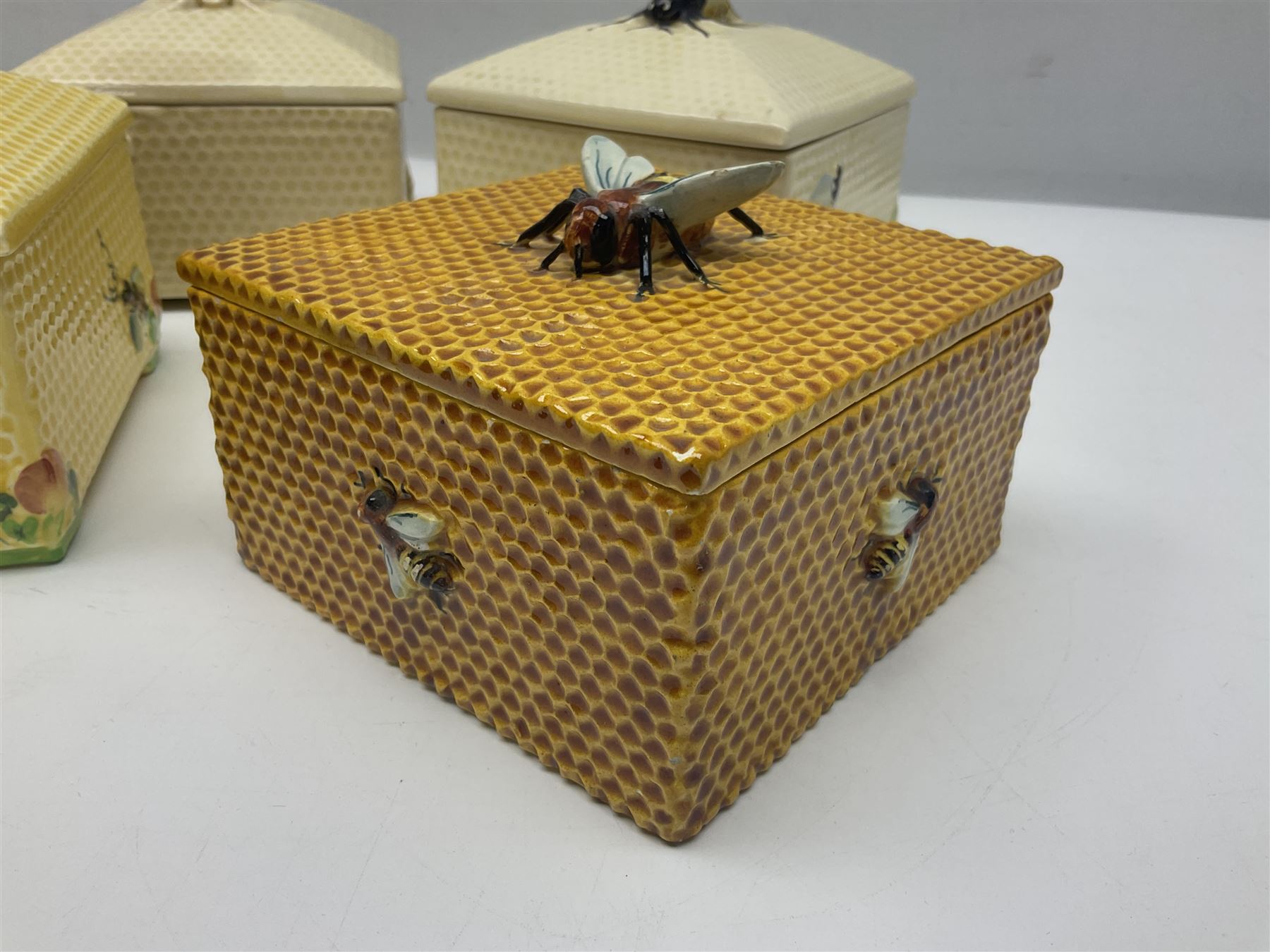 Four square honey boxes with lids,  each decorated with honeycomb pattern and finished with a bee finial