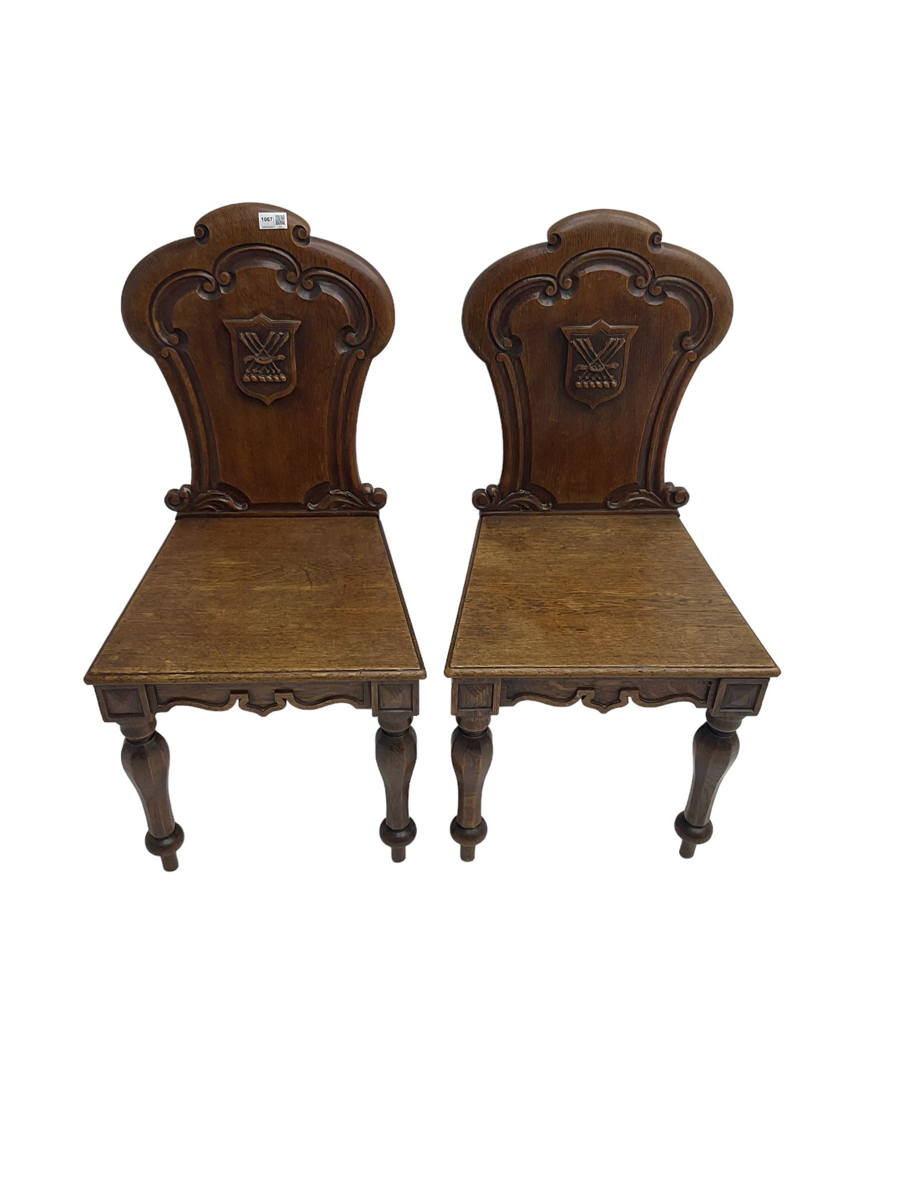 Pair Victorian oak hall chairs, scallop shaped back with carved scrolls and central shield moulding, panel seat over shaped frieze rail, raised on turned supports