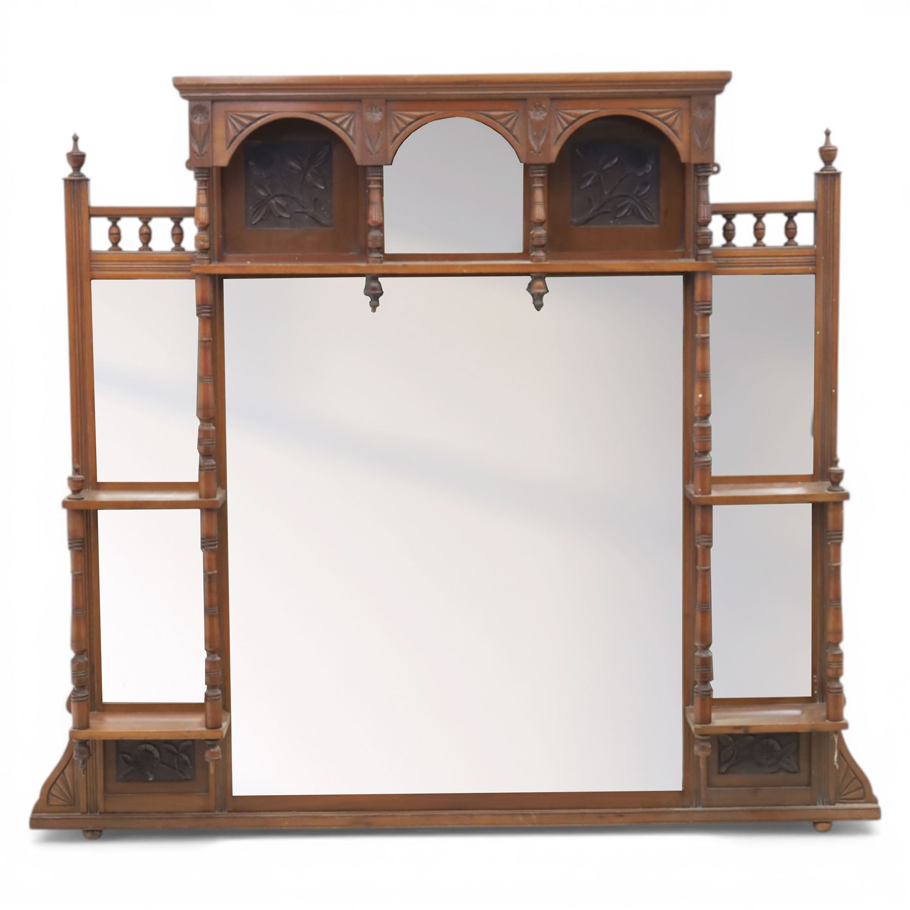 Edwardian walnut overmantel mirror, moulded cornice over three arched apertures with turned supports, flanked by open shelves with turned uprights and finials, carved foliate panels to the base