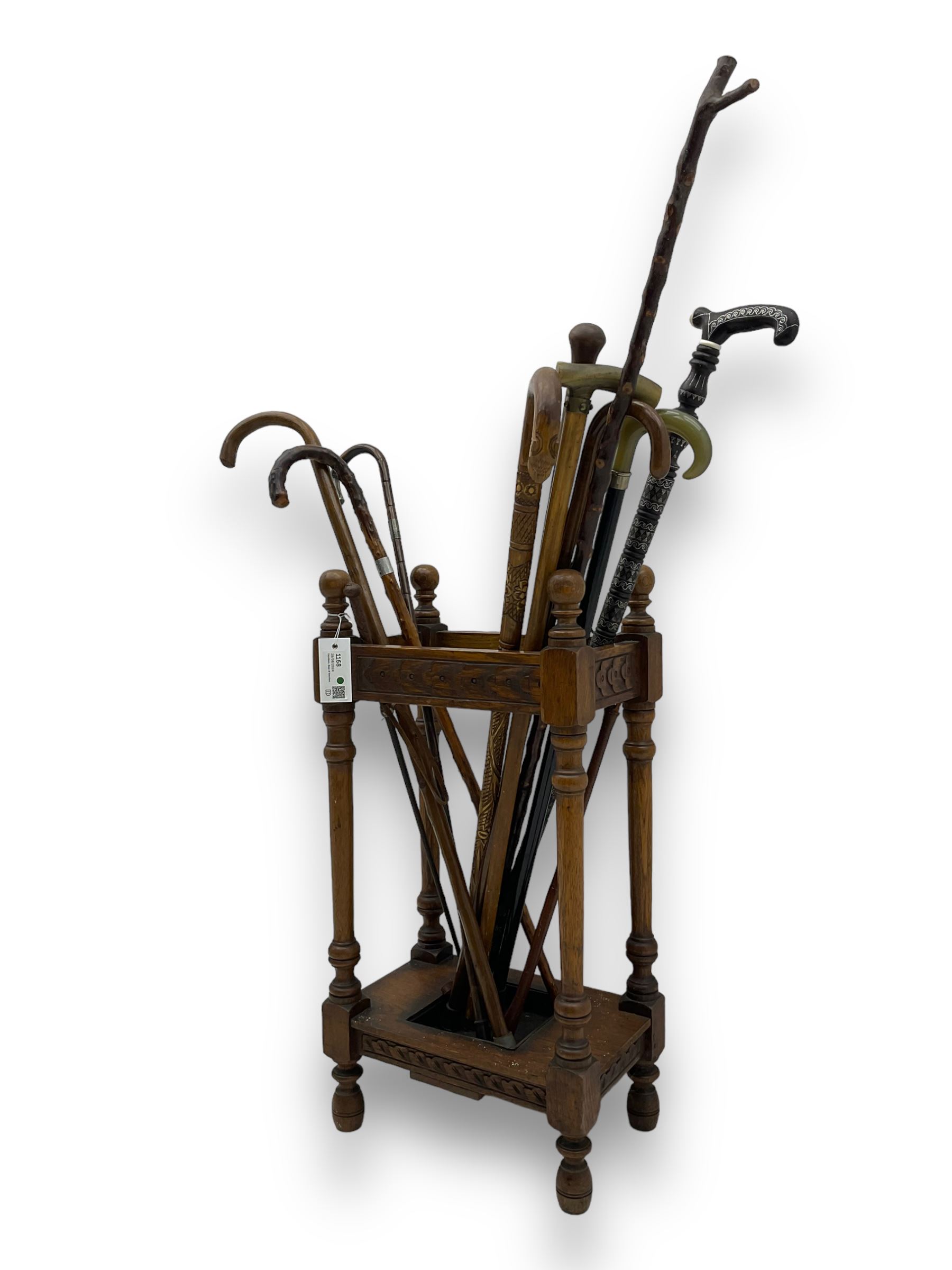 Early 20th century oak stick stand, rectangular structure with decorative carving, square base fitted with tray, on turned supports topped with finials; twelve assorted walking canes 