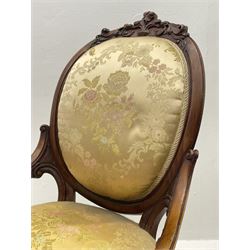 Victorian walnut lady’s drawing room chair, the cameo back cresting rail carved with scrolled foliate and central cartouche, scrolled open arms pierced and carved with flowers, upholstered in gold floral pattern fabric, serpentine sprung seat, carved cabriole supports with brass and ceramic castors 