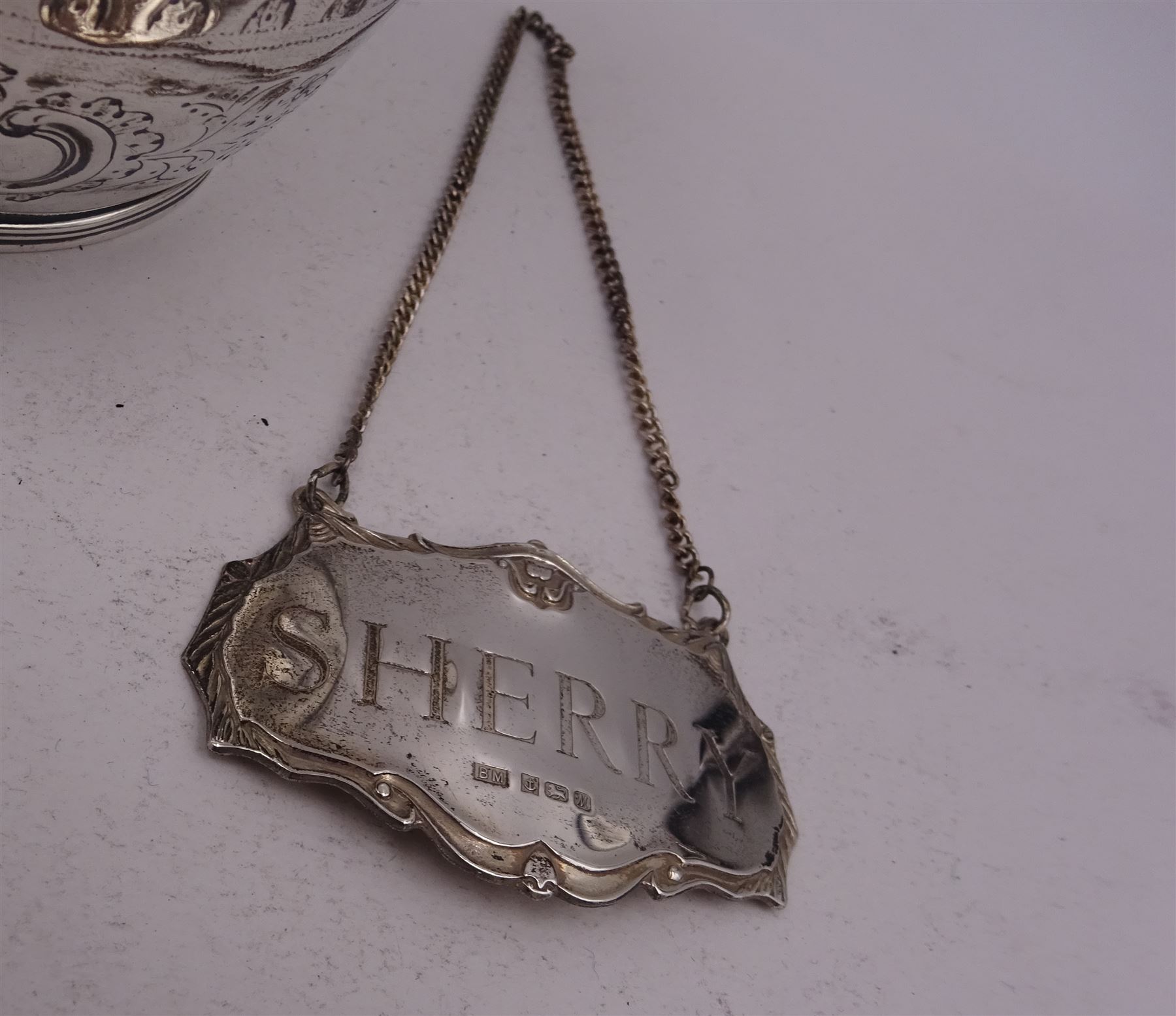 George III silver cream jug, of helmet form with angular handle, embossed with floral and scrolling decoration and engraved initial, hallmarked Edward Mayfield, London 1806, H9.3cm, together with a modern silver 'Sherry' decanter label, hallmarked Birmingham Mint, Birmingham 1986