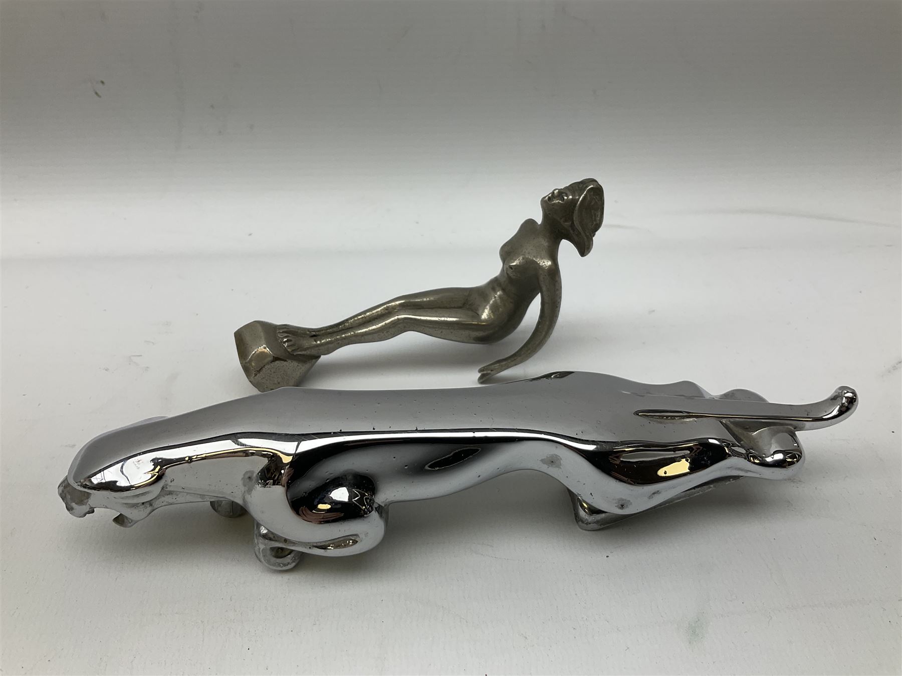Nickel plated car mascot as a nude lady in a diving pose, similar to an A.E. Lejeune 'Speed Nymph', but marked 'N.L.C. Co. RegEd Des.'; chrome leaping Jaguar car mascot; and quantity of car model name letters, numbers and logos including Mercedes-Benz etc