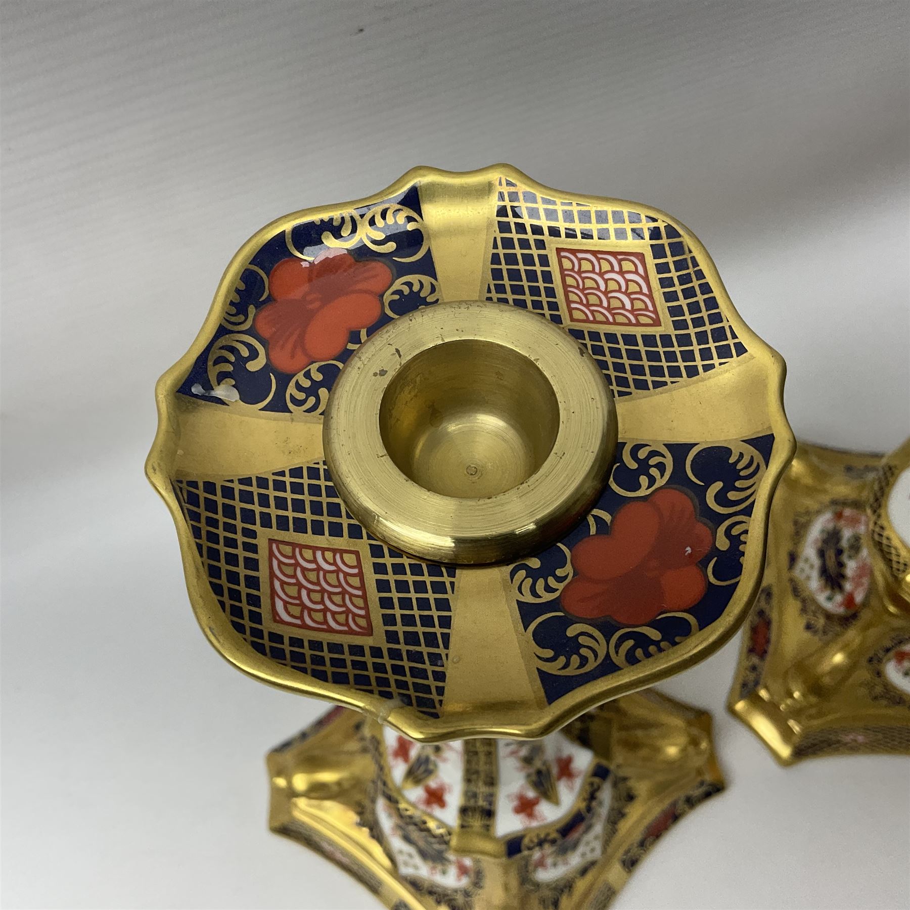 Pair of modern Royal Crown Derby Old Imari 1128 pattern candlesticks, each with shaped drip tray affixed to squat socket, upon spreading stem and canted square base with gilt dolphin edges, with printed marks beneath including Roman numeral year cypher for 2003, H26.5cm, with original boxes