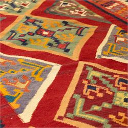South West Persian Qashqai flatweave kilim, madder red ground with stacked diamond panels filled with latch hook and angular floral motifs, enclosed by multiple geometric borders in palettes of indigo, green, and ochre 